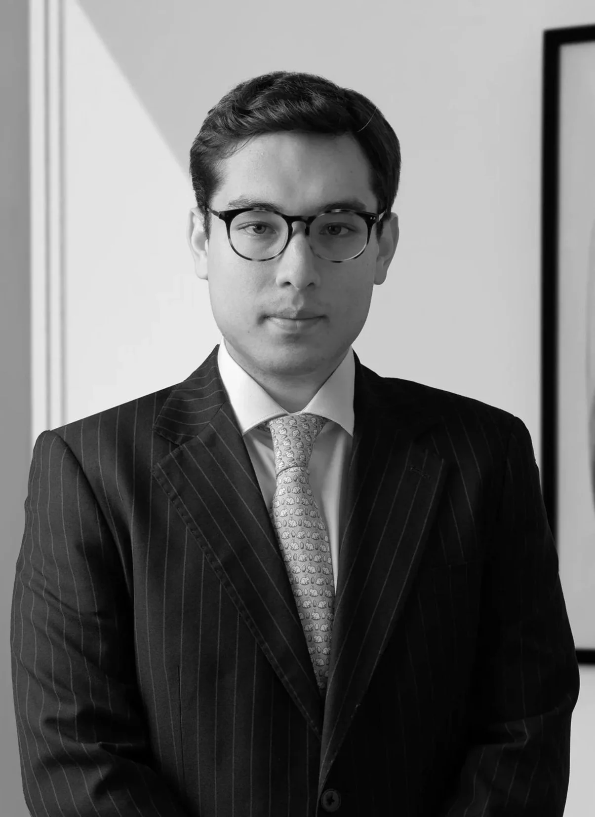 Hombre con gafas, cabello oscuro, ropa formal y fondo de oficina.