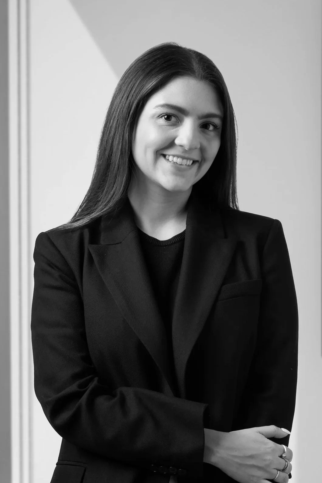 Retrato en blanco y negro de una mujer con cabello largo y oscuro, vestida con saco negro, sonriendo, con fondo gris.