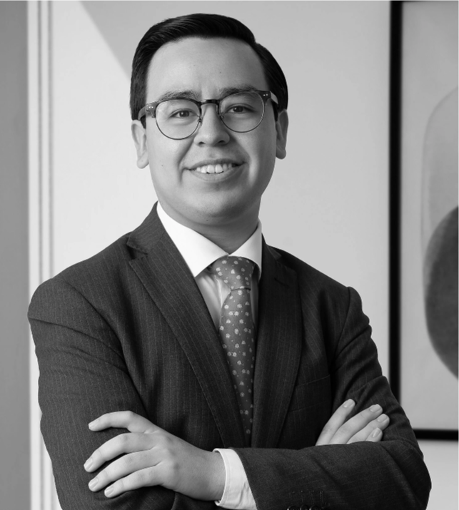 Hombre con gafas, traje y corbata en un entorno interior, de aspecto profesional y sonriente.