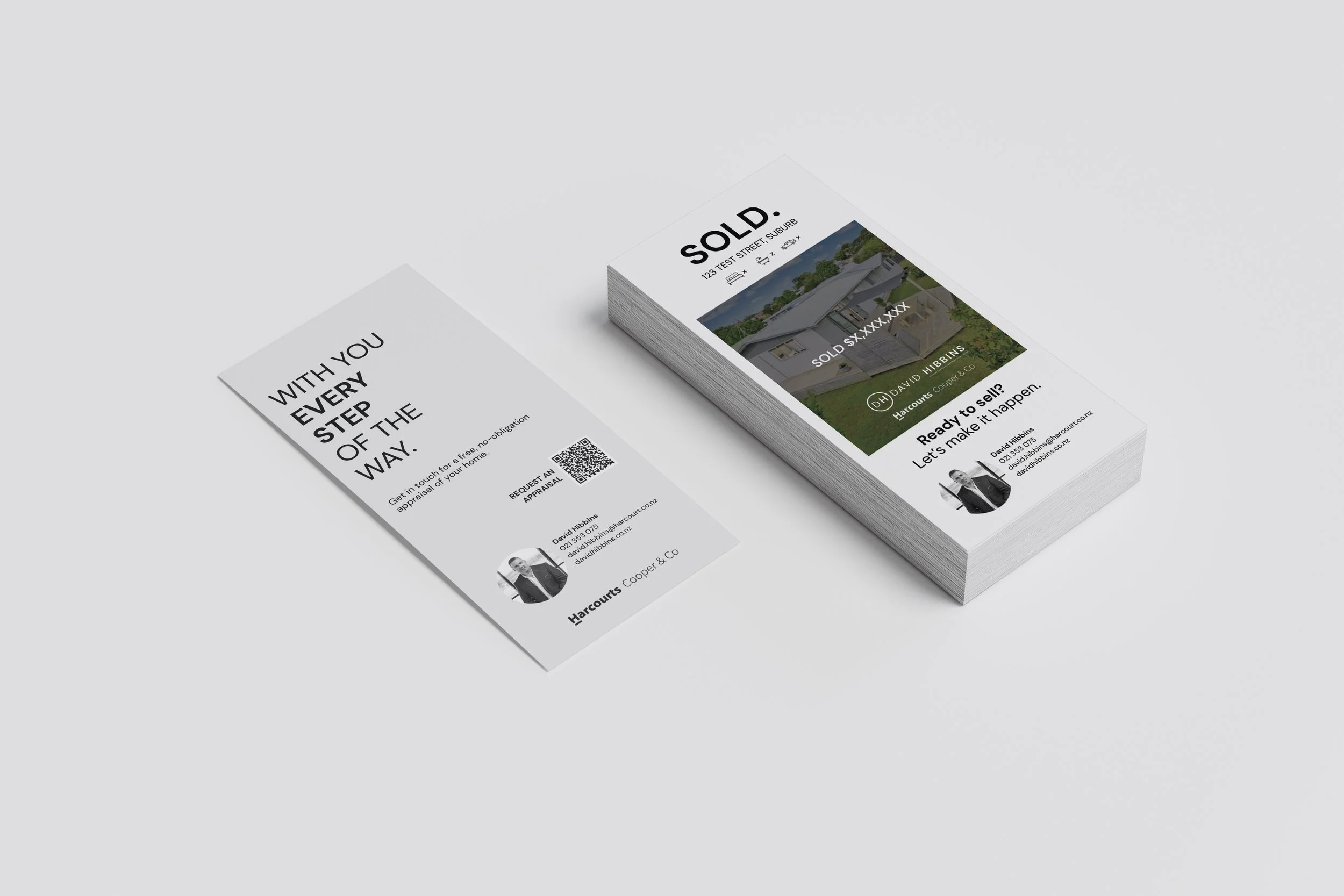 Stack of real estate sold flyers showing a house, contact information, and a QR code, placed on a white surface.