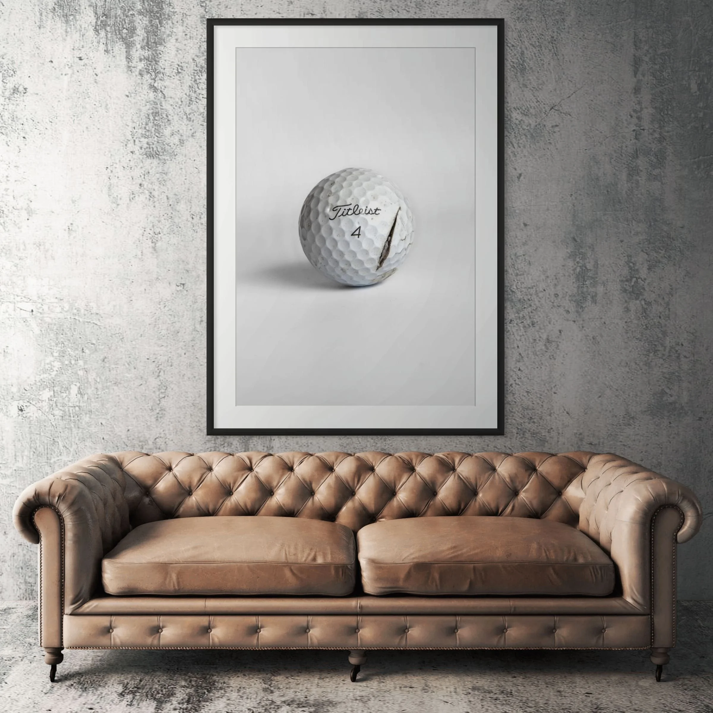 Titleist Pro V1 clean cracked golf ball framed print displayed above tan leather sofa in living room