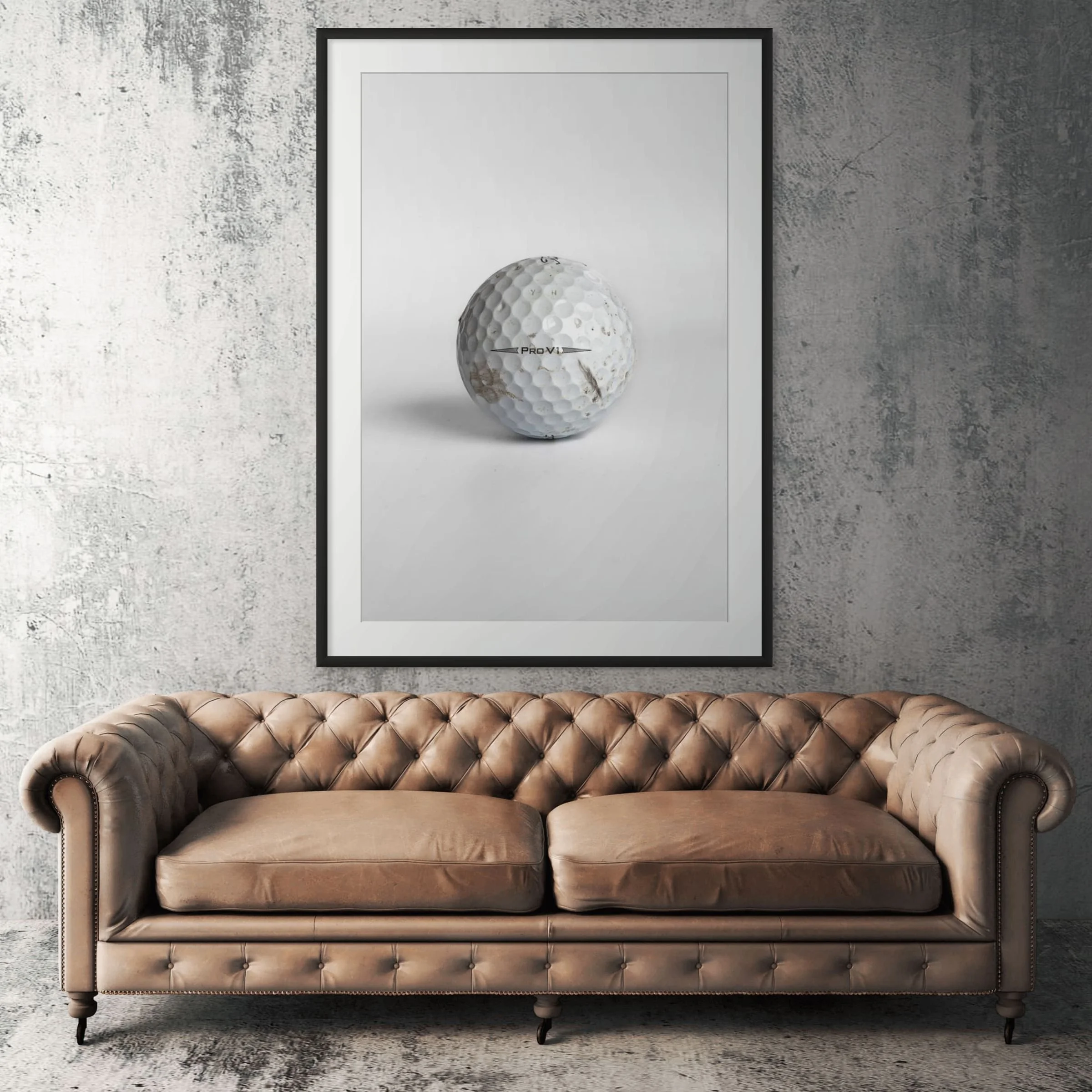 Titleist Pro V1 scuffed golf ball framed print displayed above tan leather sofa in living room