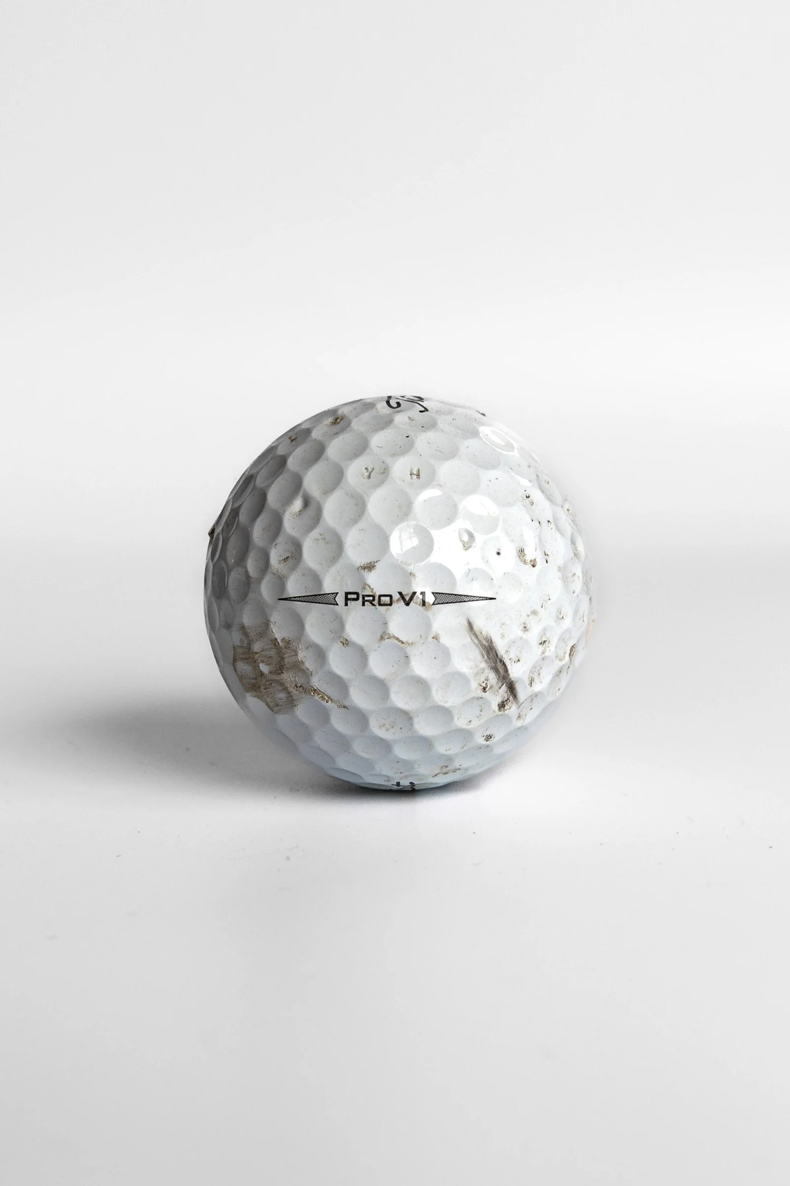 Titleist Pro V1 scuffed golf ball with dirt and wear marks white background