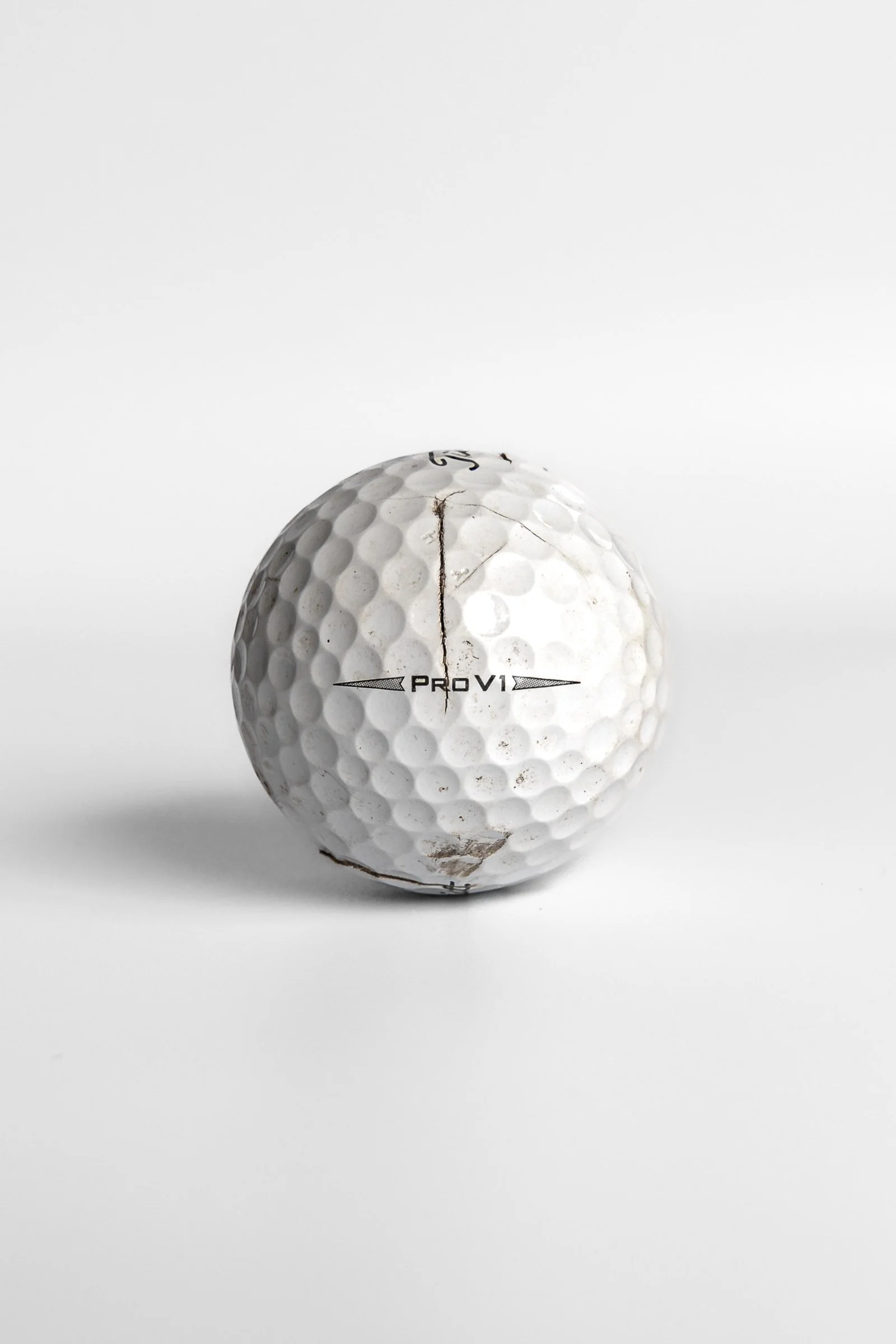 Titleist Pro V1 split golf ball with vertical crack and dirt marks white background