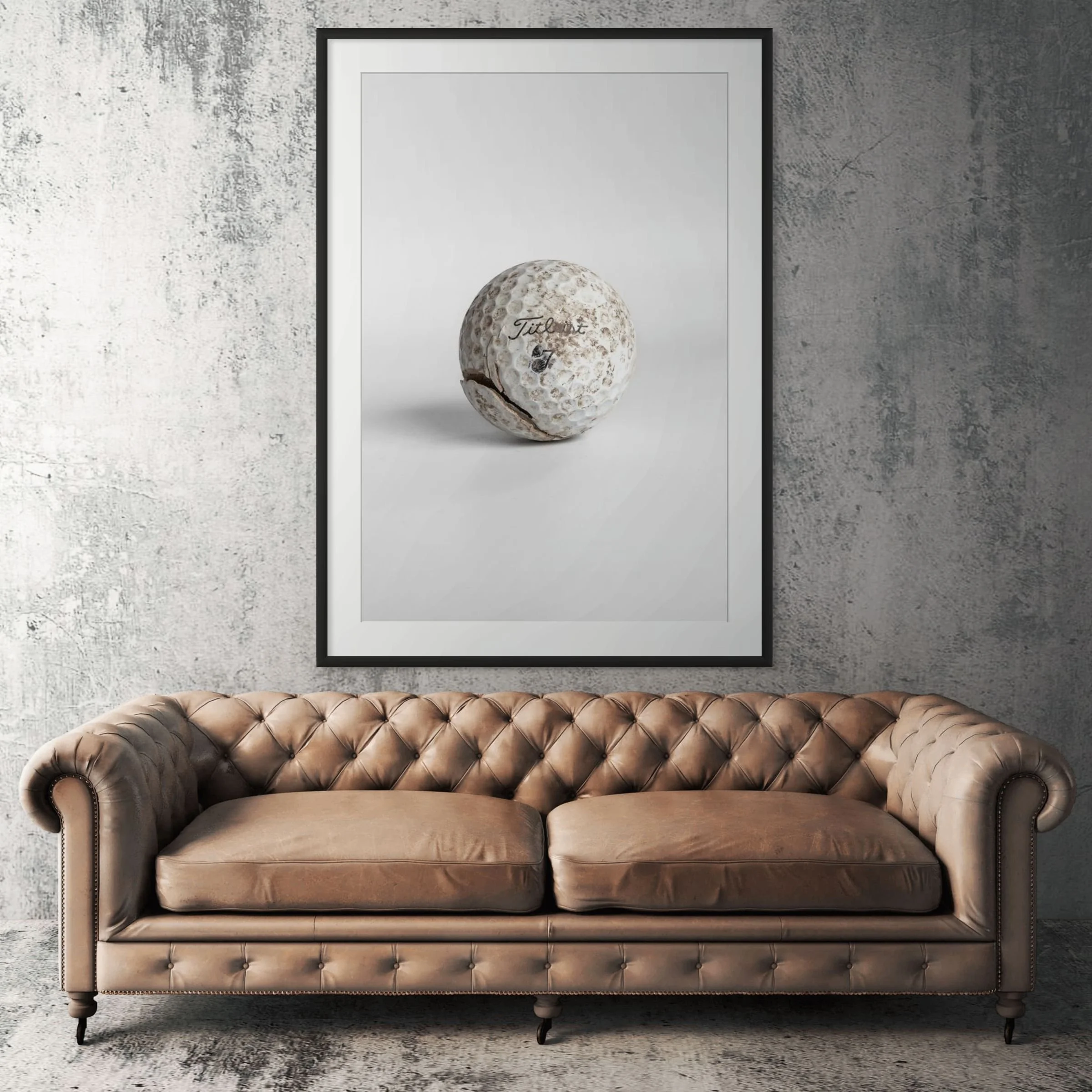 Titleist Pro V1 worn golf ball framed print displayed above tan leather sofa in living room