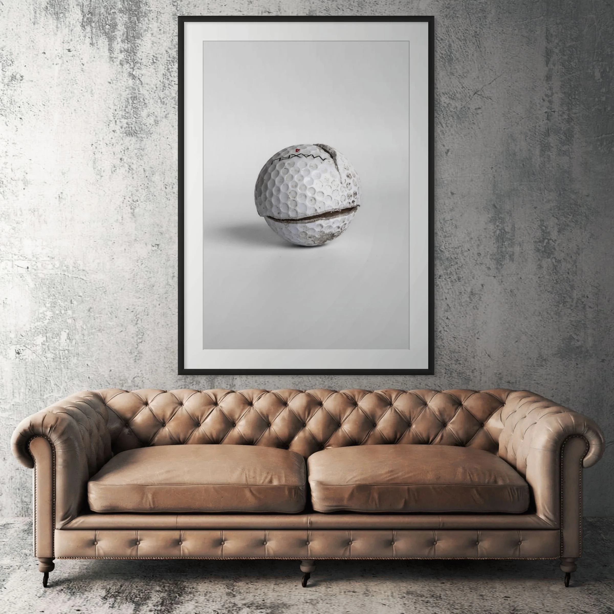 Maxfli Revolution cracked golf ball framed print displayed above tan leather sofa in living room