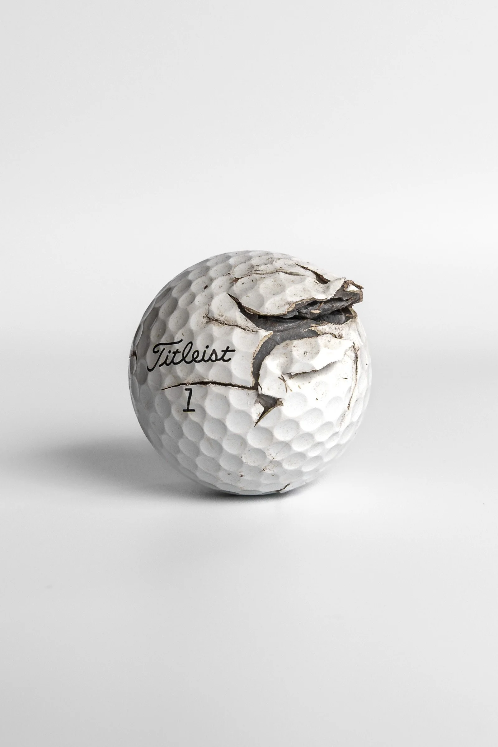Titleist Pro V1 fractured golf ball showing impact damage white background
