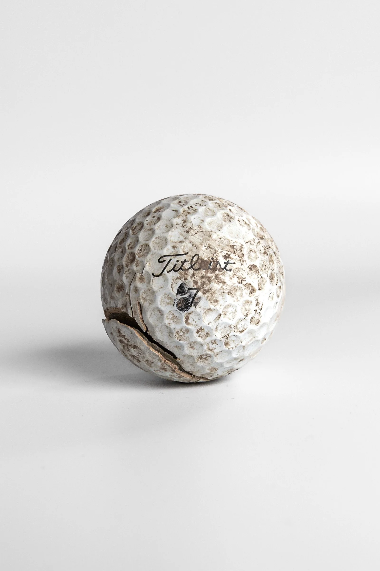 Titleist Pro V1 worn golf ball with scuff marks and dirt white background