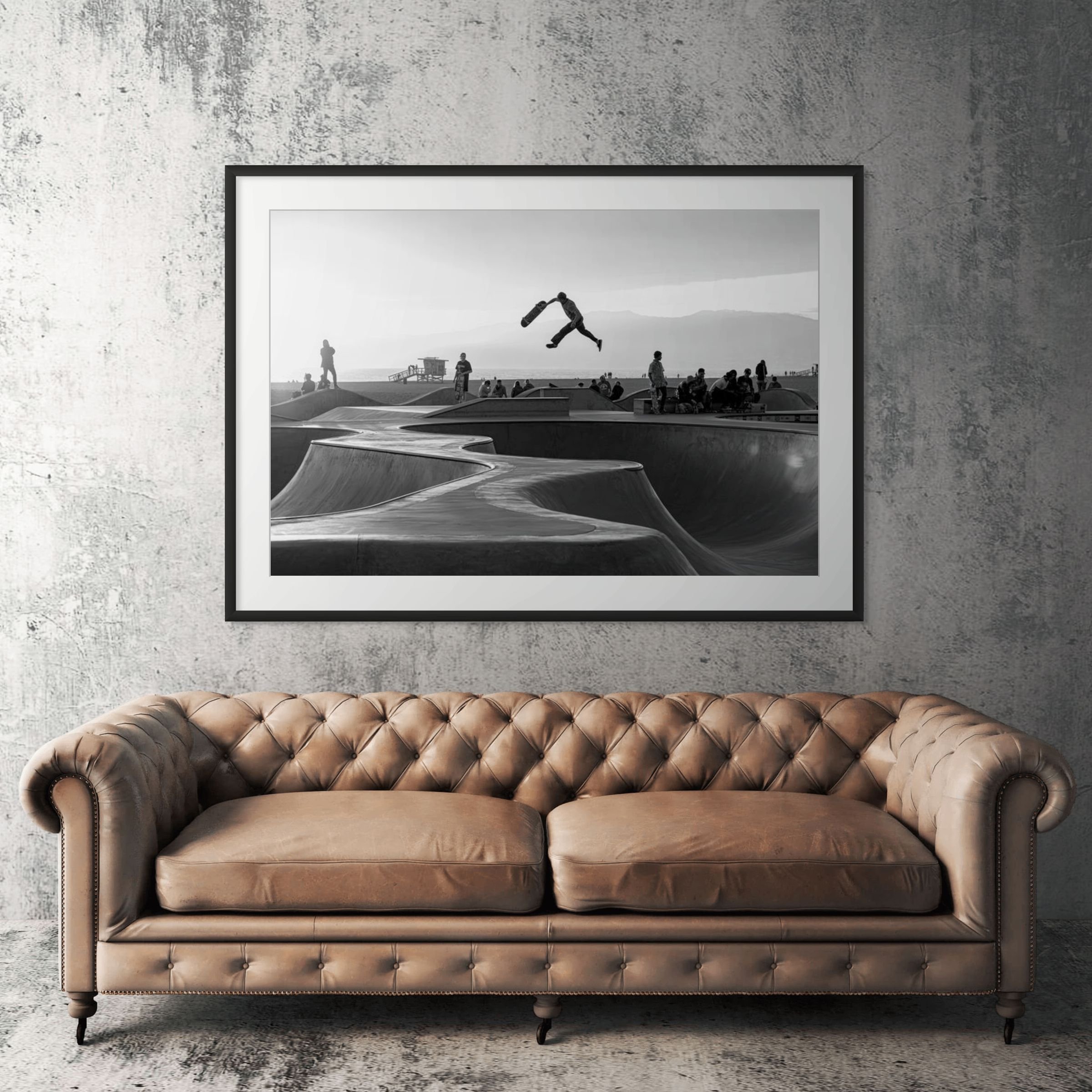 Venice Beach skateboarding black and white framed print displayed above tan leather sofa in living room