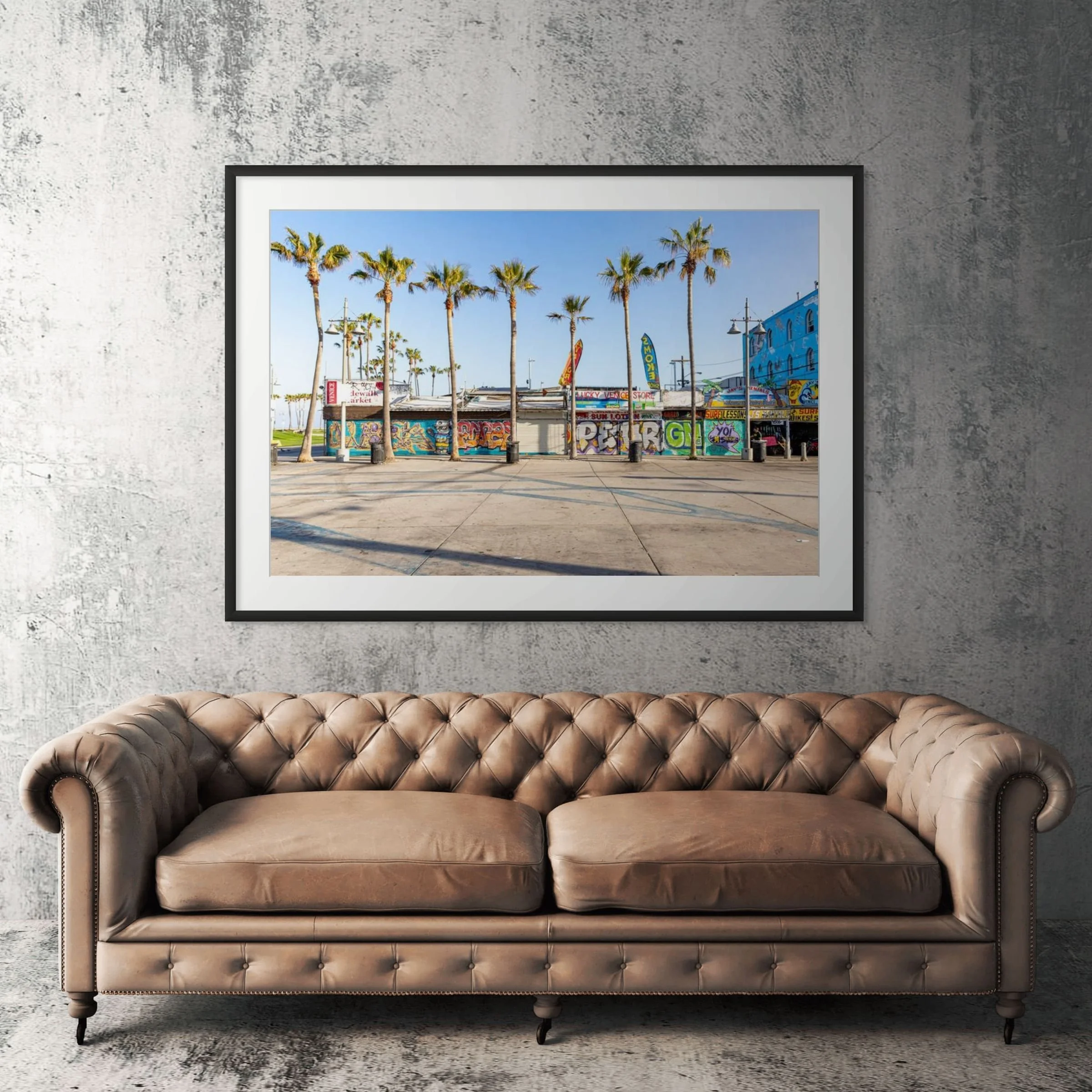 Venice Beach boardwalk framed print displayed above tan leather sofa in living room