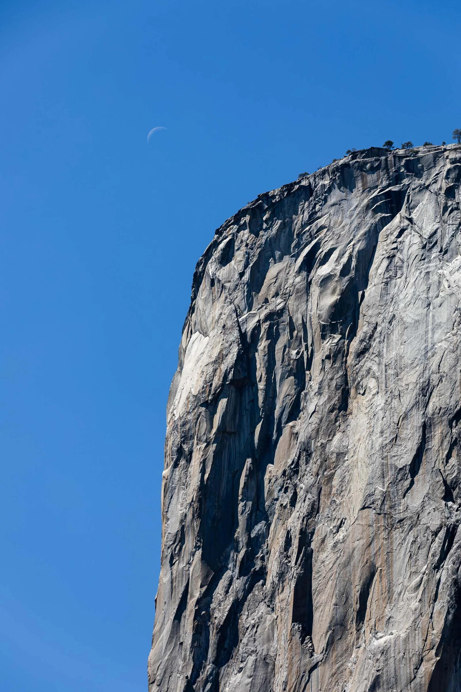 Yosemite El Capitan massive granite cliff face with blue sky and crescent moon California
