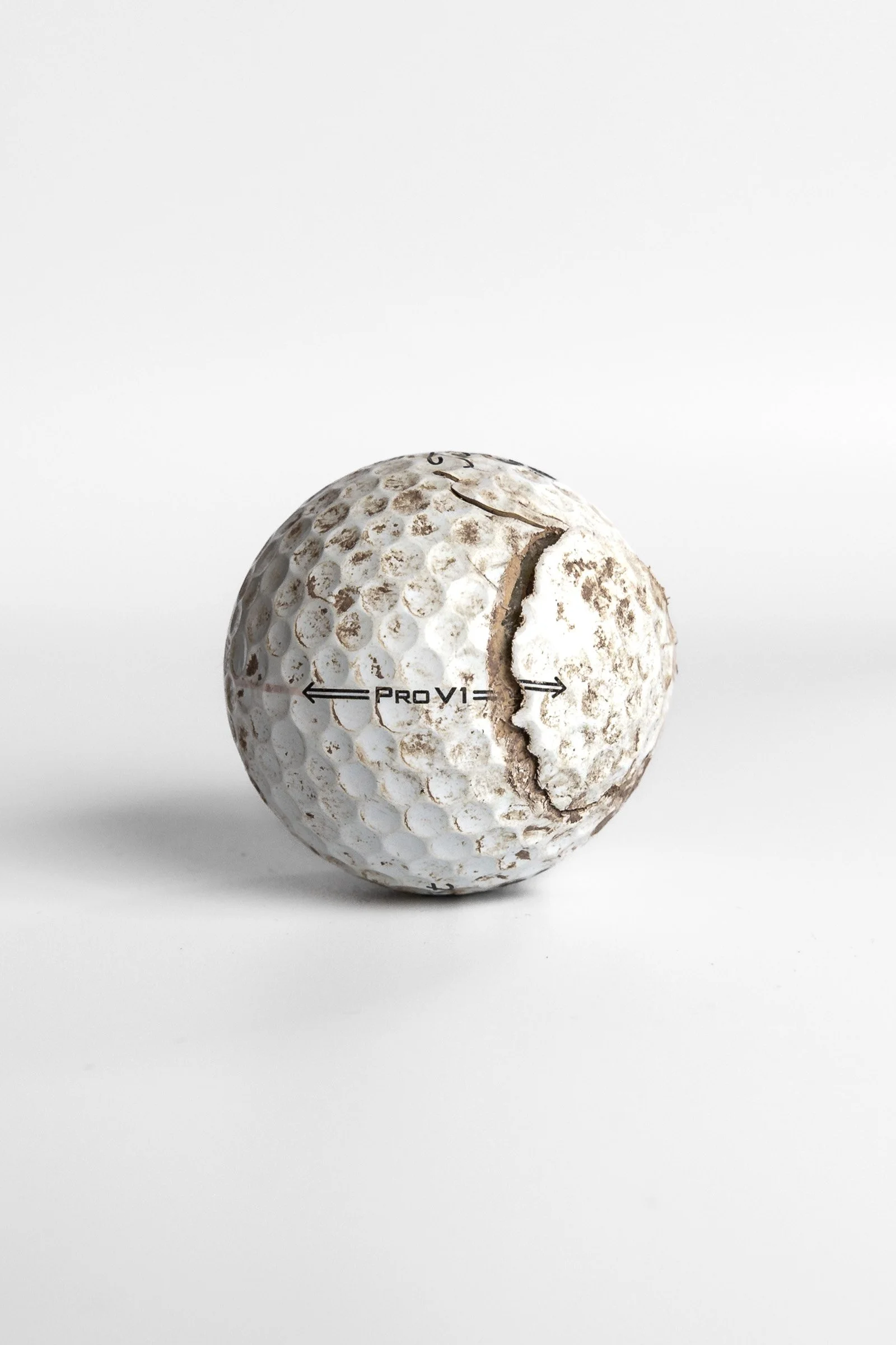 Titleist Pro V1 aged golf ball with vertical crack and dirt marks white background