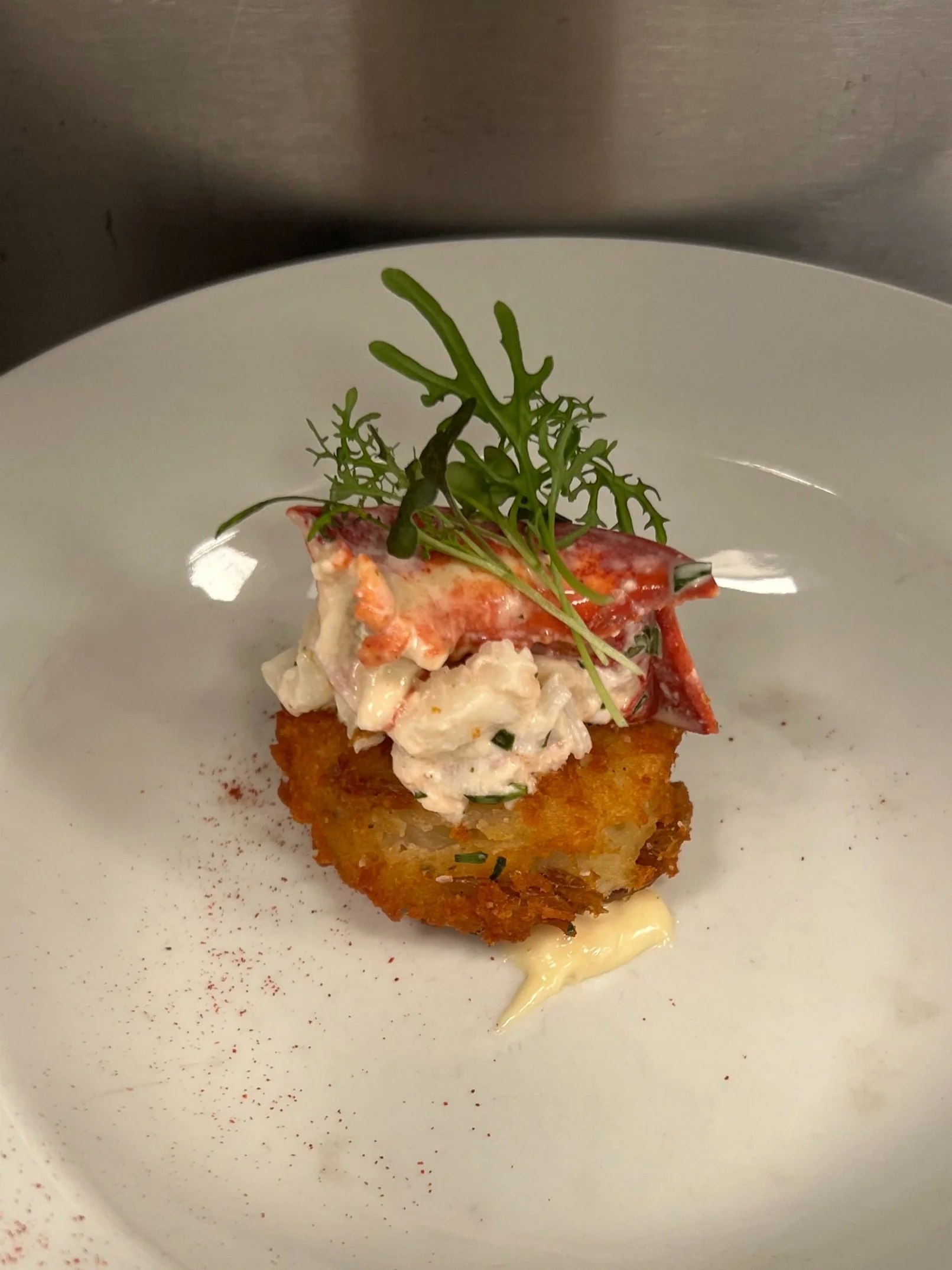 A plated appetizer with a crispy base, topped with salad, a piece of lobster meat, and garnished with greens.