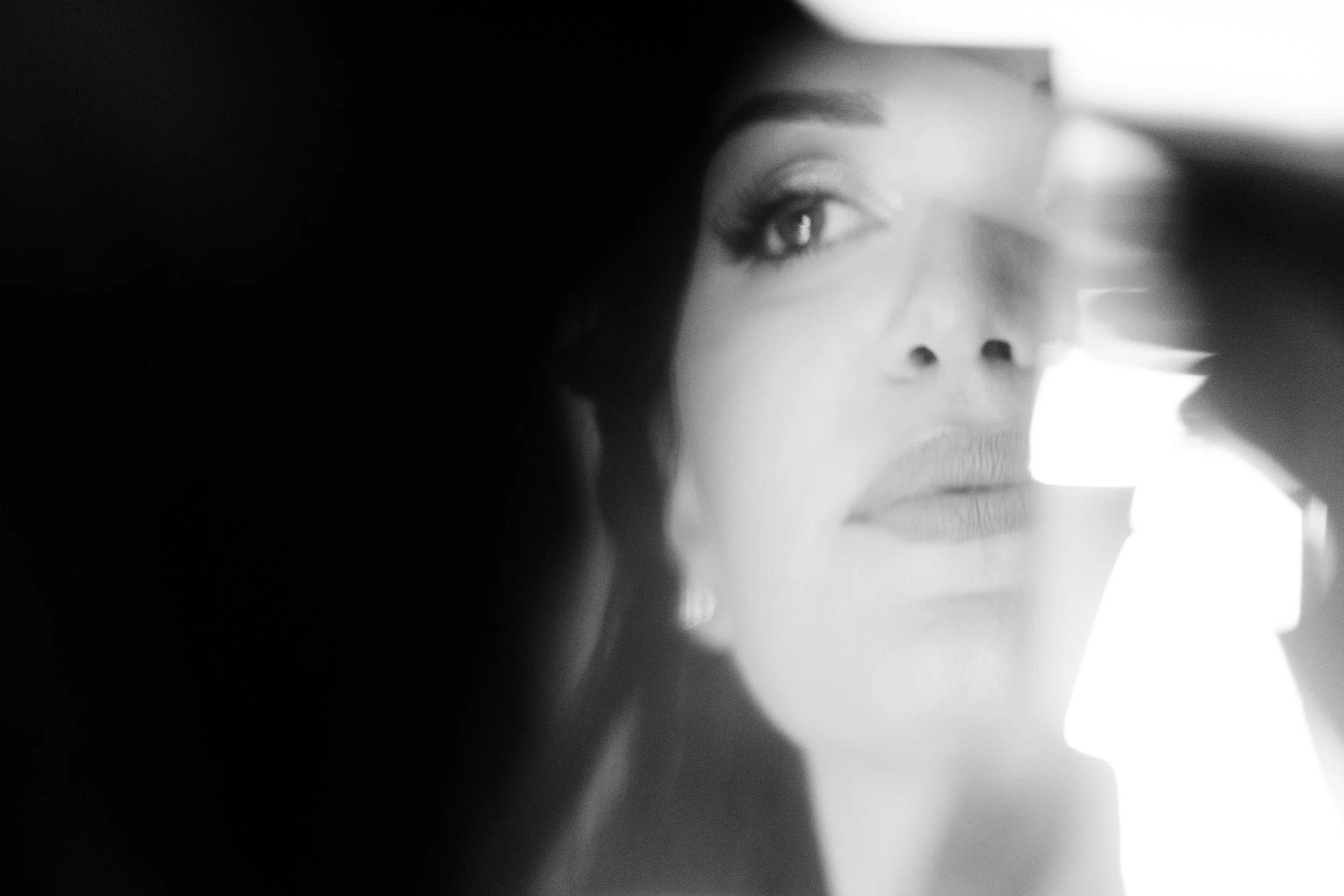 Ritratto in bianco e nero di una donna con trucco leggero, vista parziale attraverso una fessura, con luce che illumina il suo volto