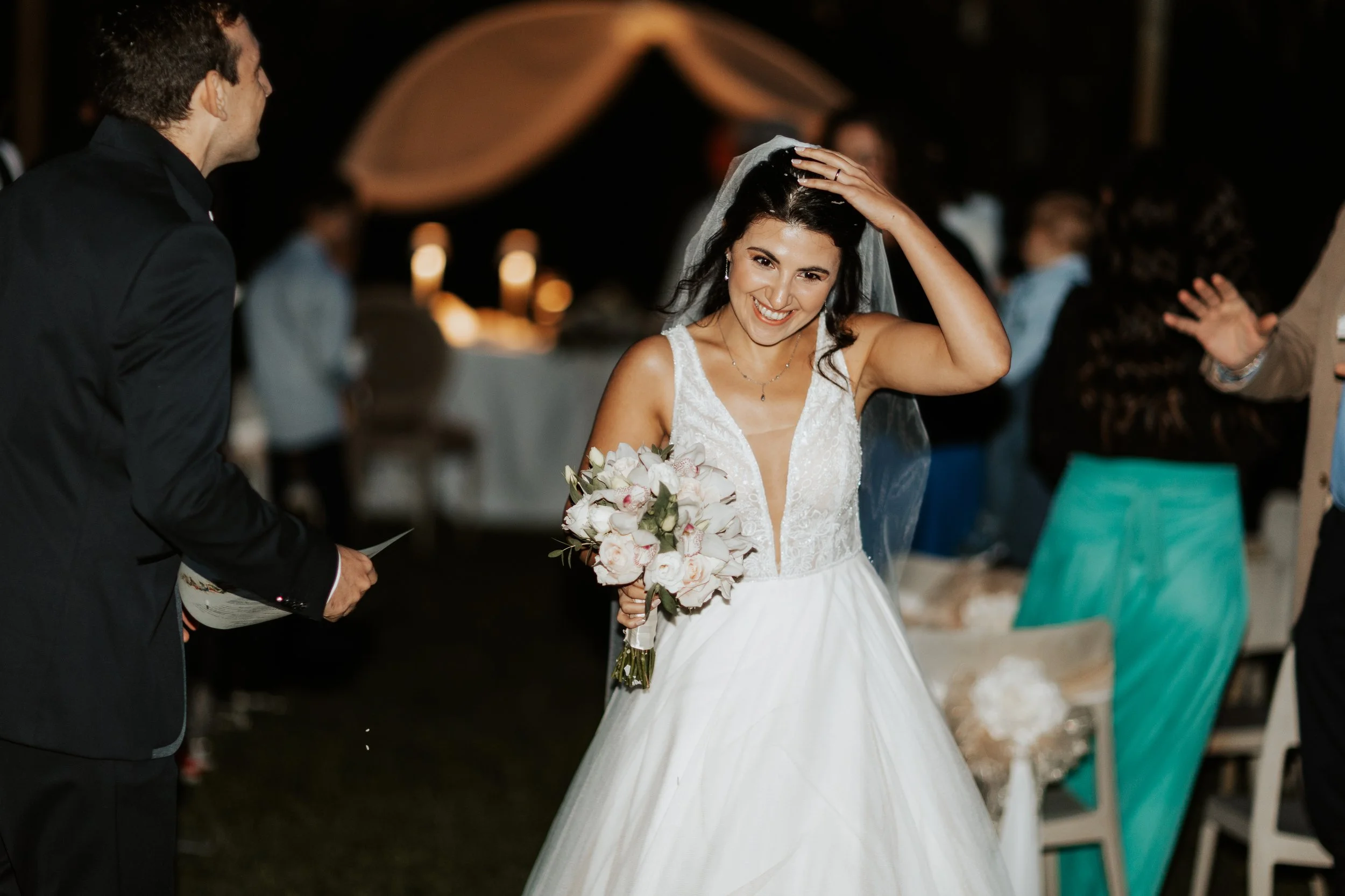 Sposa sorridente con abito da matrimonio, che tiene un bouquet di fiori, durante il ricevimento di nozze