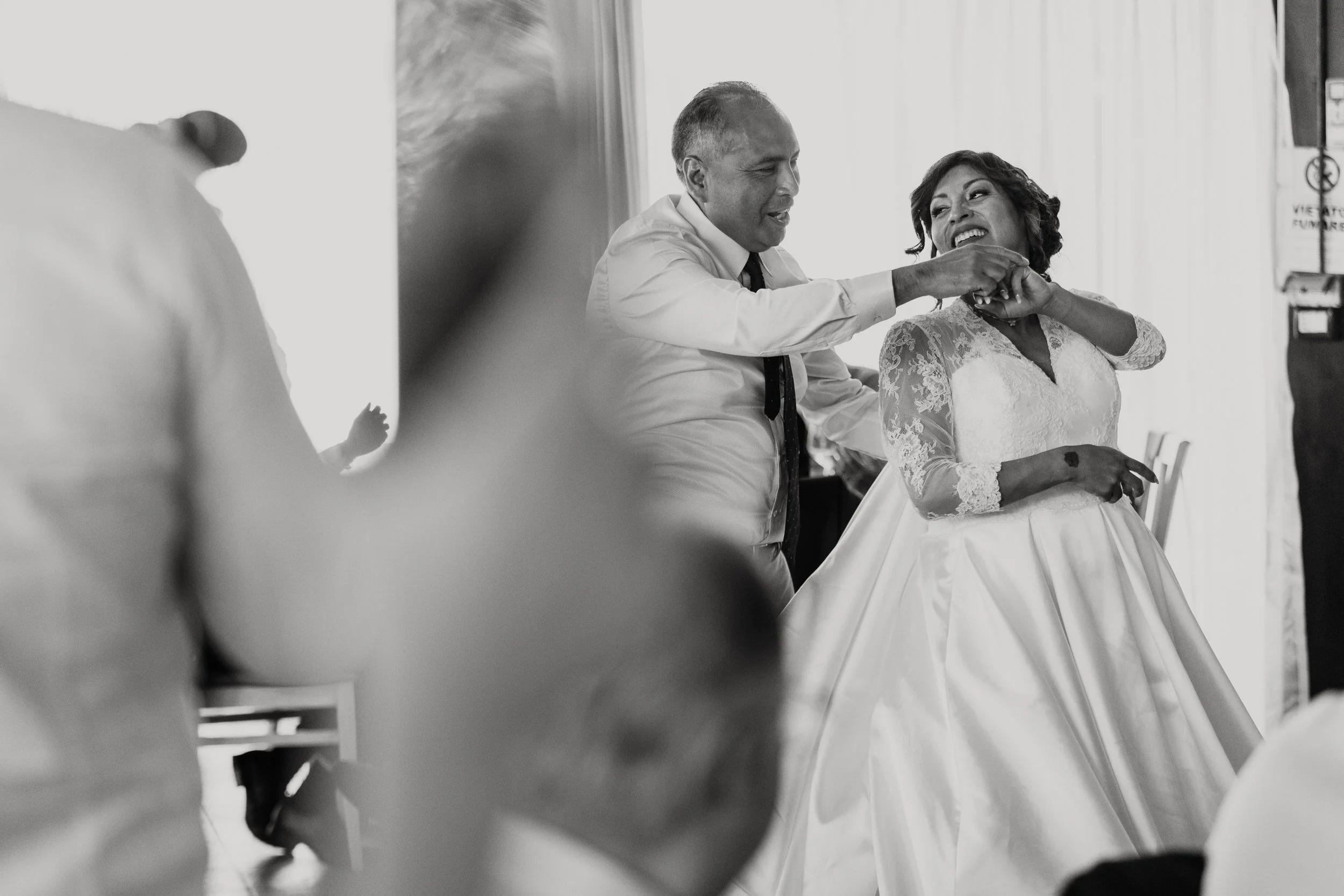 Una coppia si diverte durante il matrimonio, con l'uomo che gioca con la donna nella sala. La donna indossa un vestito da sposa con dettagli in pizzo.