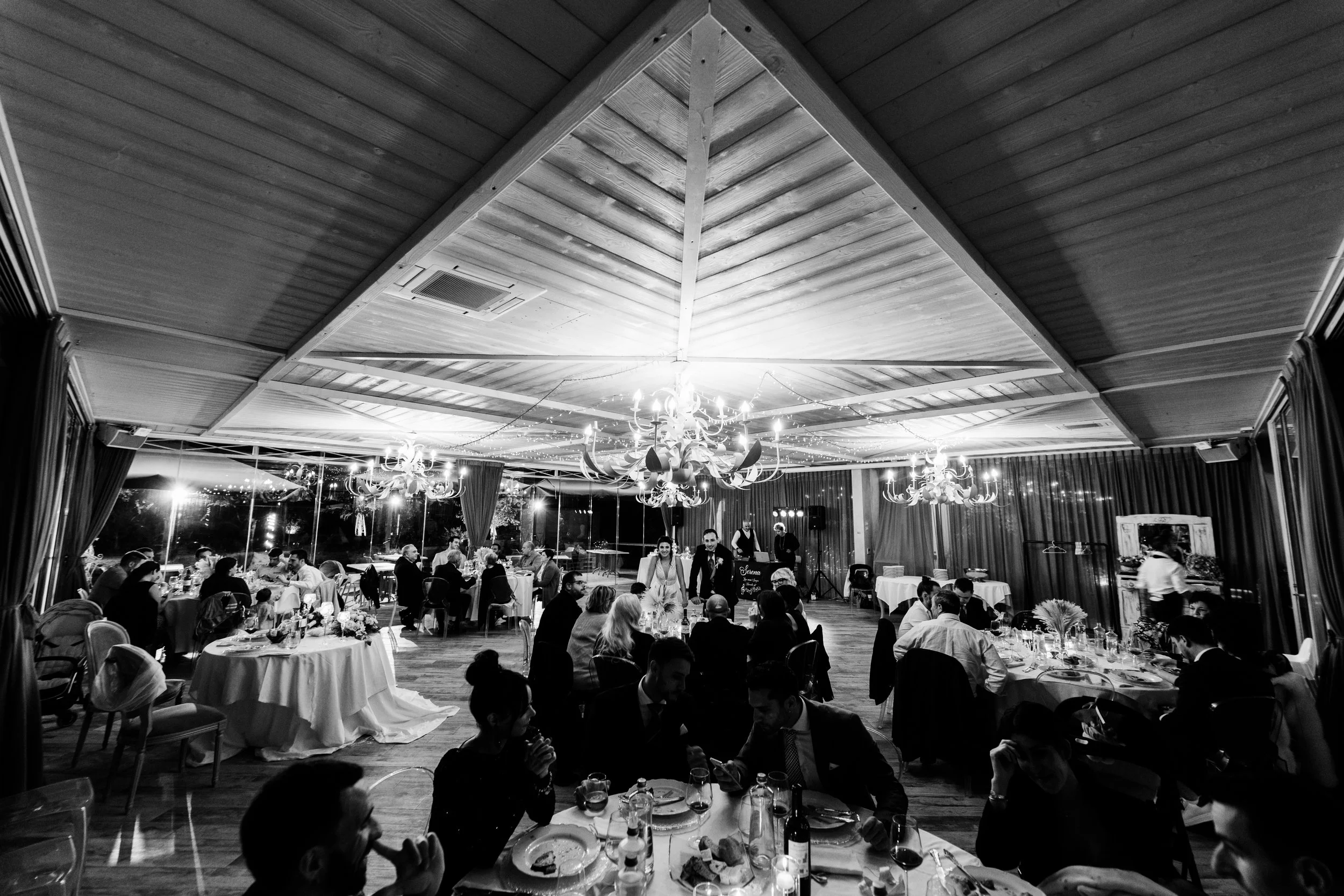 Foto di un ricevimento di matrimonio in un grande salone elegantemente arredato, con tavoli decorati e lampadari.