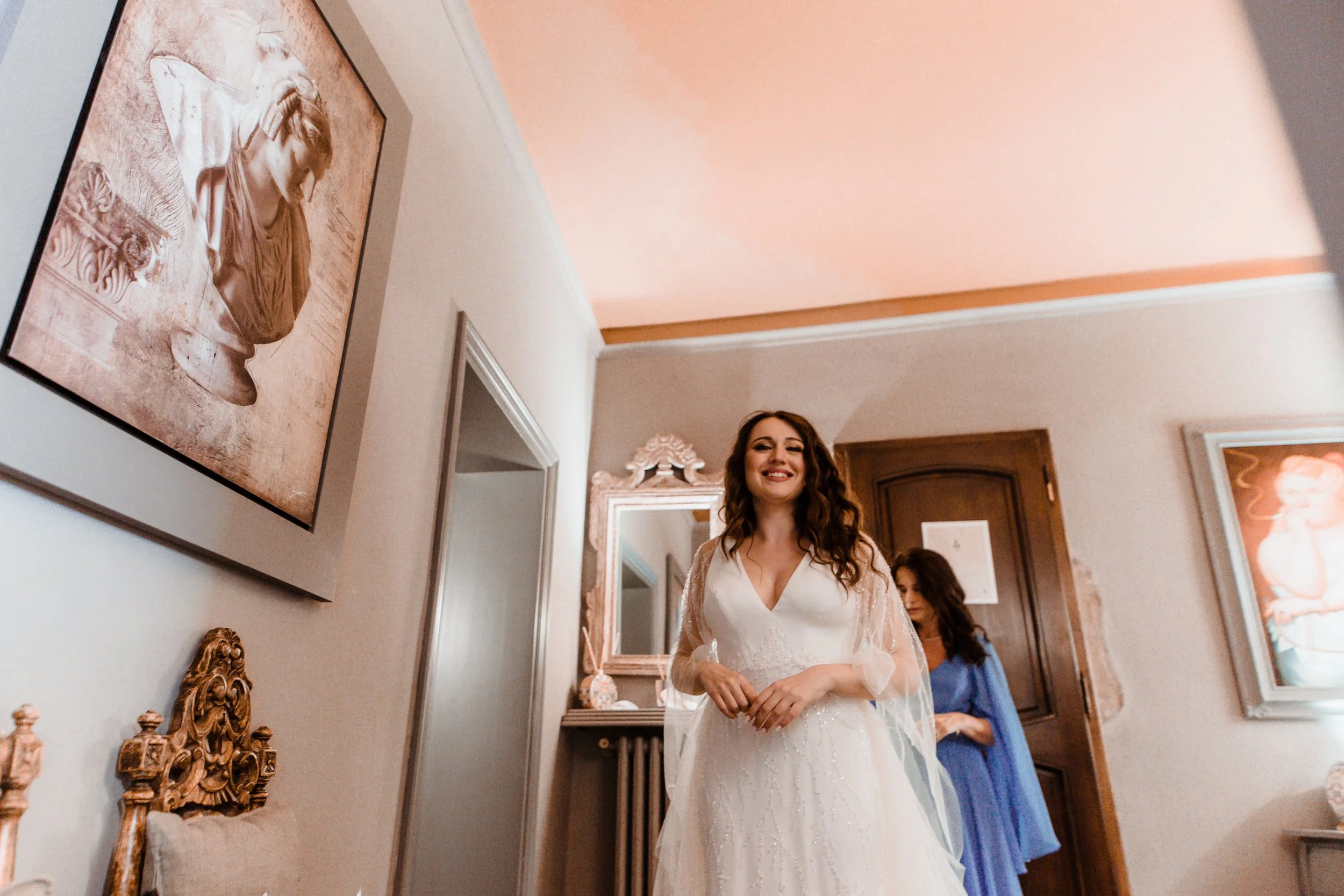 Una donna in abito da sposa sorride mentre ti trovi in una stanza decorata con quadri e mobili classici.