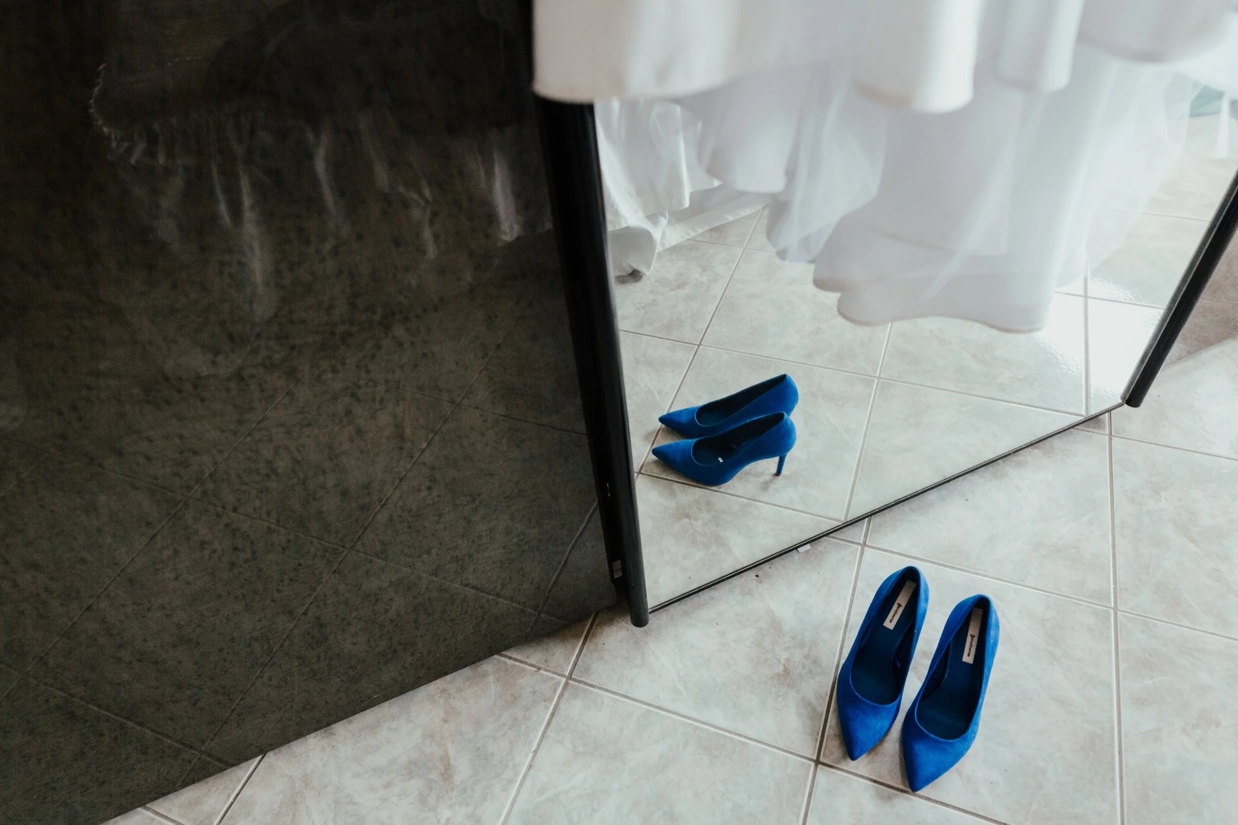 Scarpe blu di tacchi alti riflesso in uno specchio davanti a un abito bianco sospeso