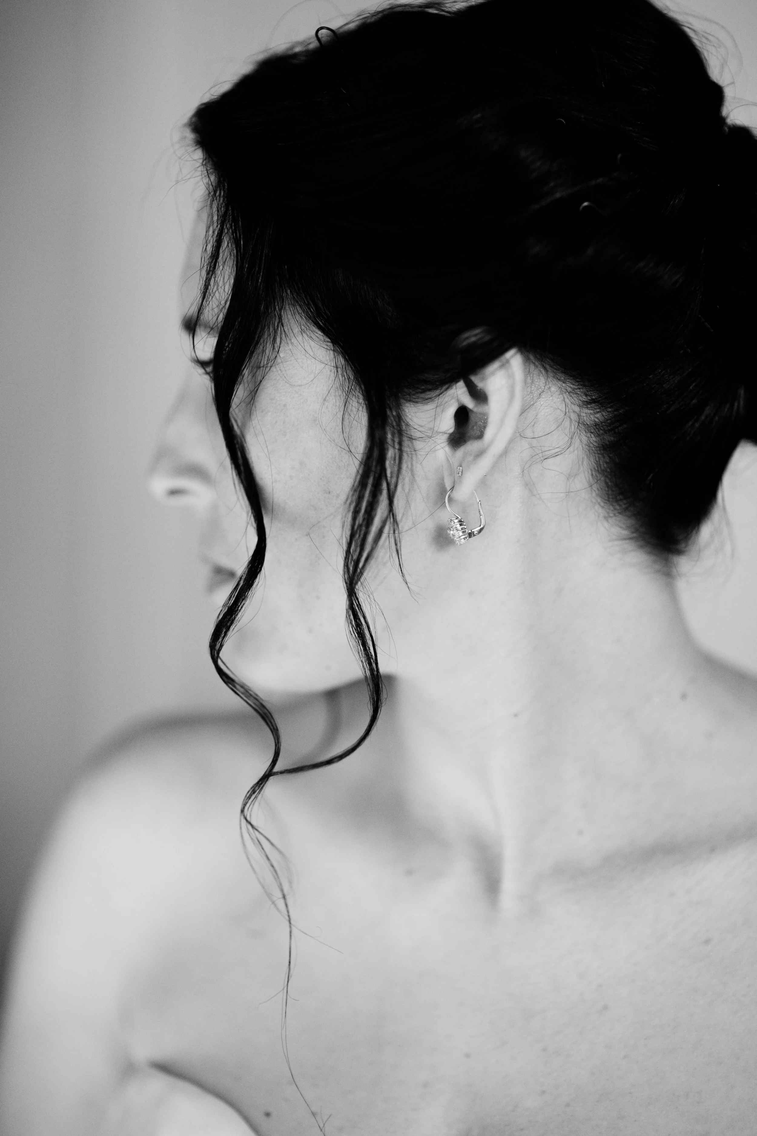 Ritratto in bianco e nero di una donna con capelli scuri acconciati raccolti, con una ciocca che le cade sul volto, che indossa un orecchino a cerchio con pietra brillante.