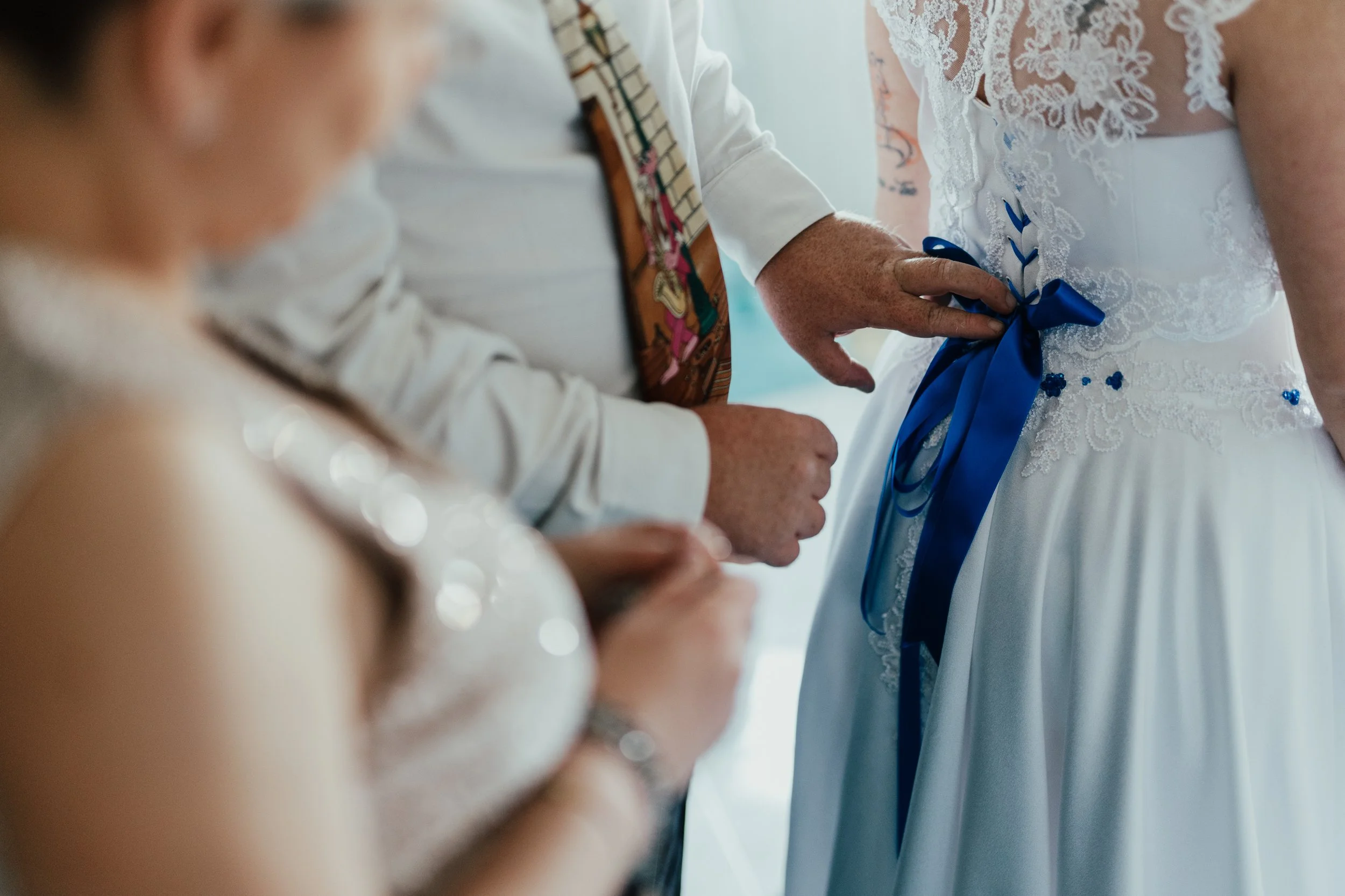 Dettaglio di una cerimonia di matrimonio con sposa che indossa un abito con fiocco blu e altre persone con abiti eleganti