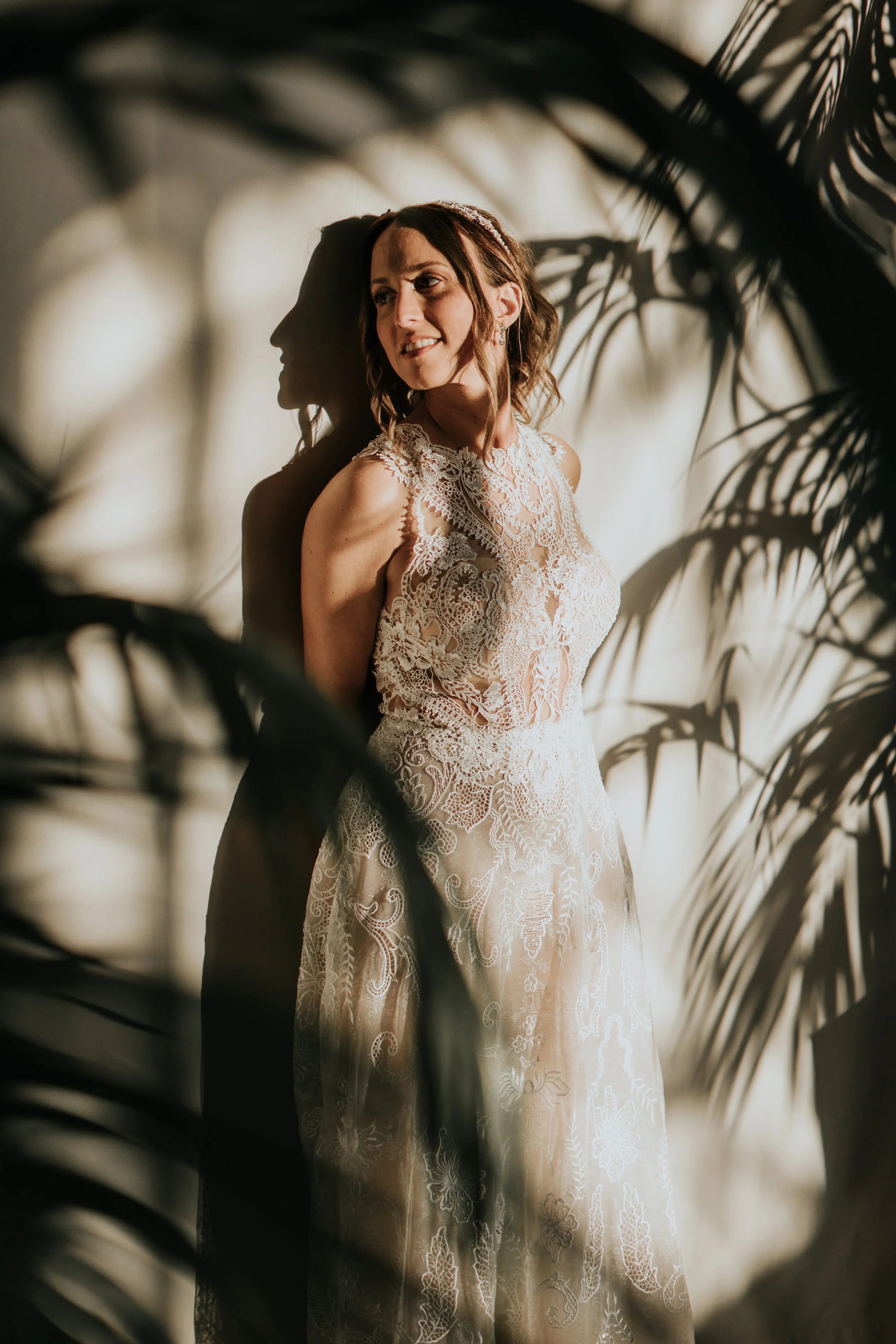 Donna in abito da sposa con luci calde e foglie scure sullo sfondo.