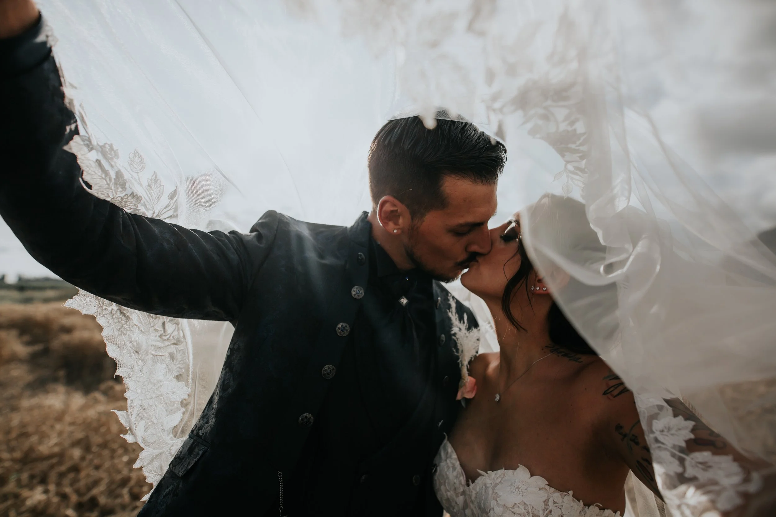 Gli sposi si baciano sotto il velo di un matrimonio, in un campo all'aperto con albe soffuse.