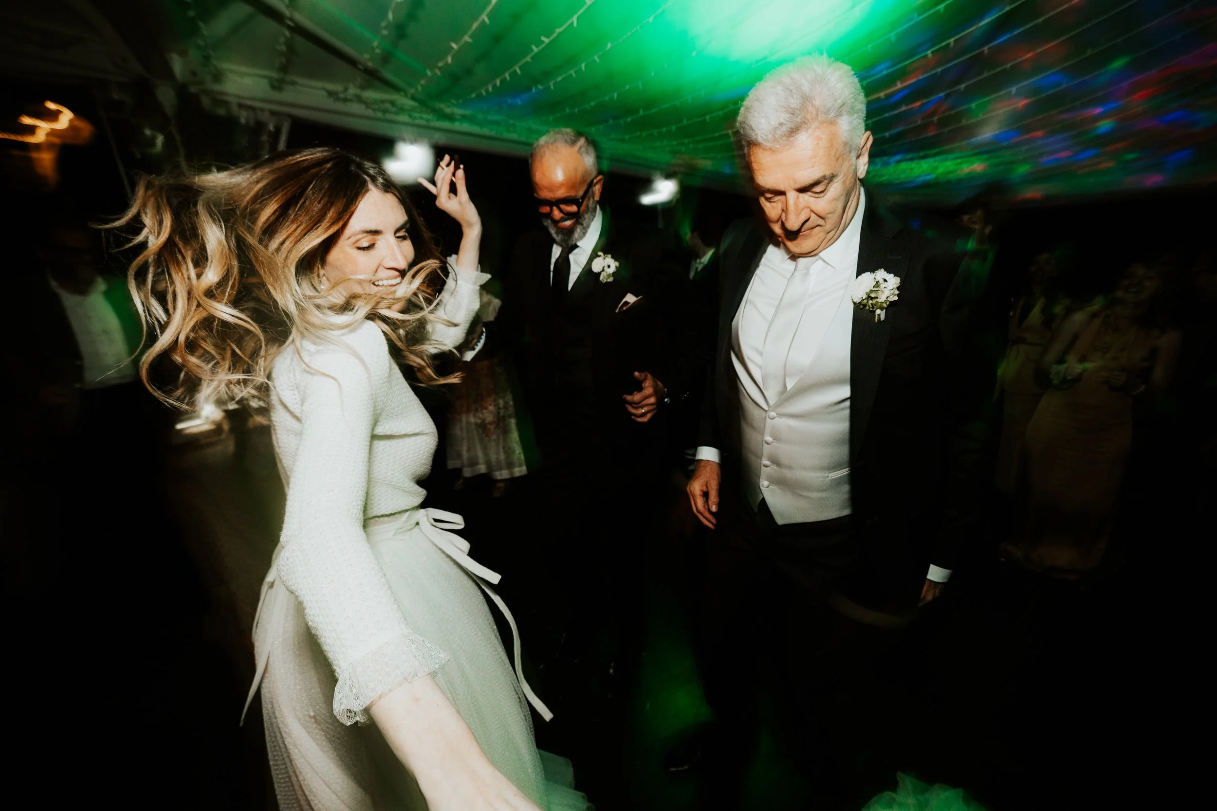 Persone che ballano e sorridono a una festa, decorazioni e luci colorate sul soffitto.