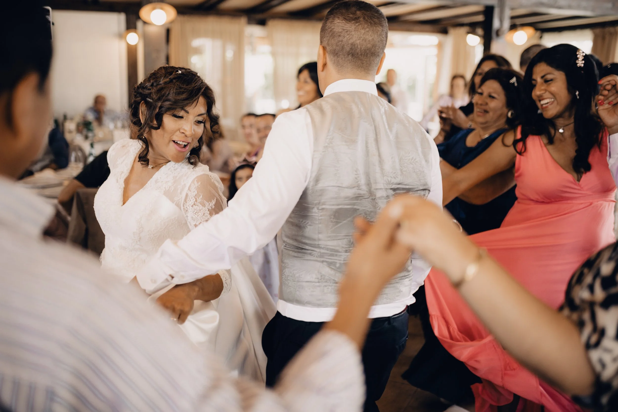 Married couple dancing during a celebration surrounded by guests in a warmly lit venue.