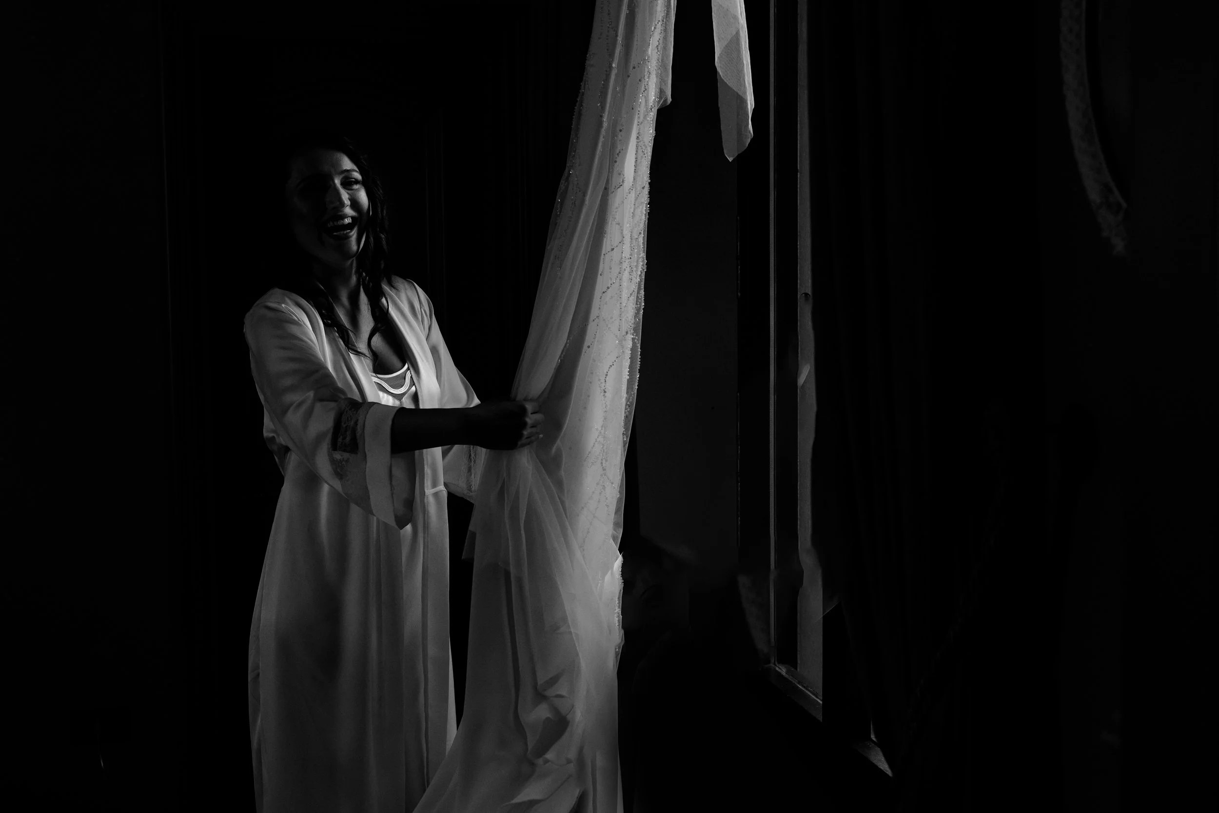 Donna in abiti da notte che sorride mentre si prepara davanti a una finestra con una tenda di pizzo.