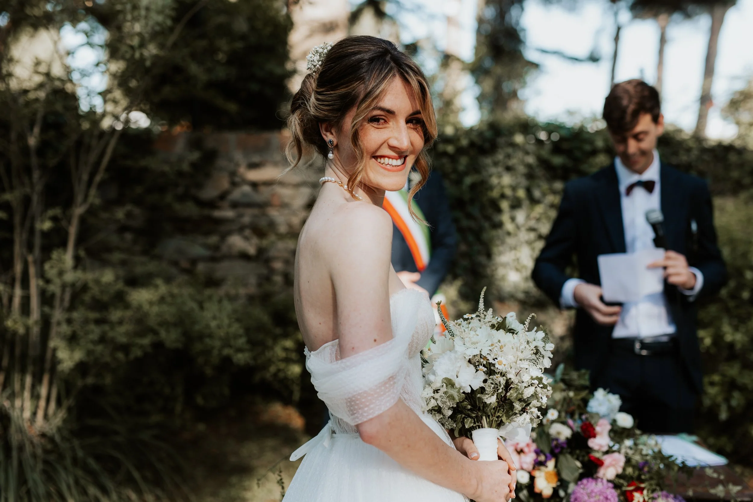 Sposa sorridente con bouquet di fiori, durante un matrimonio all'aperto.