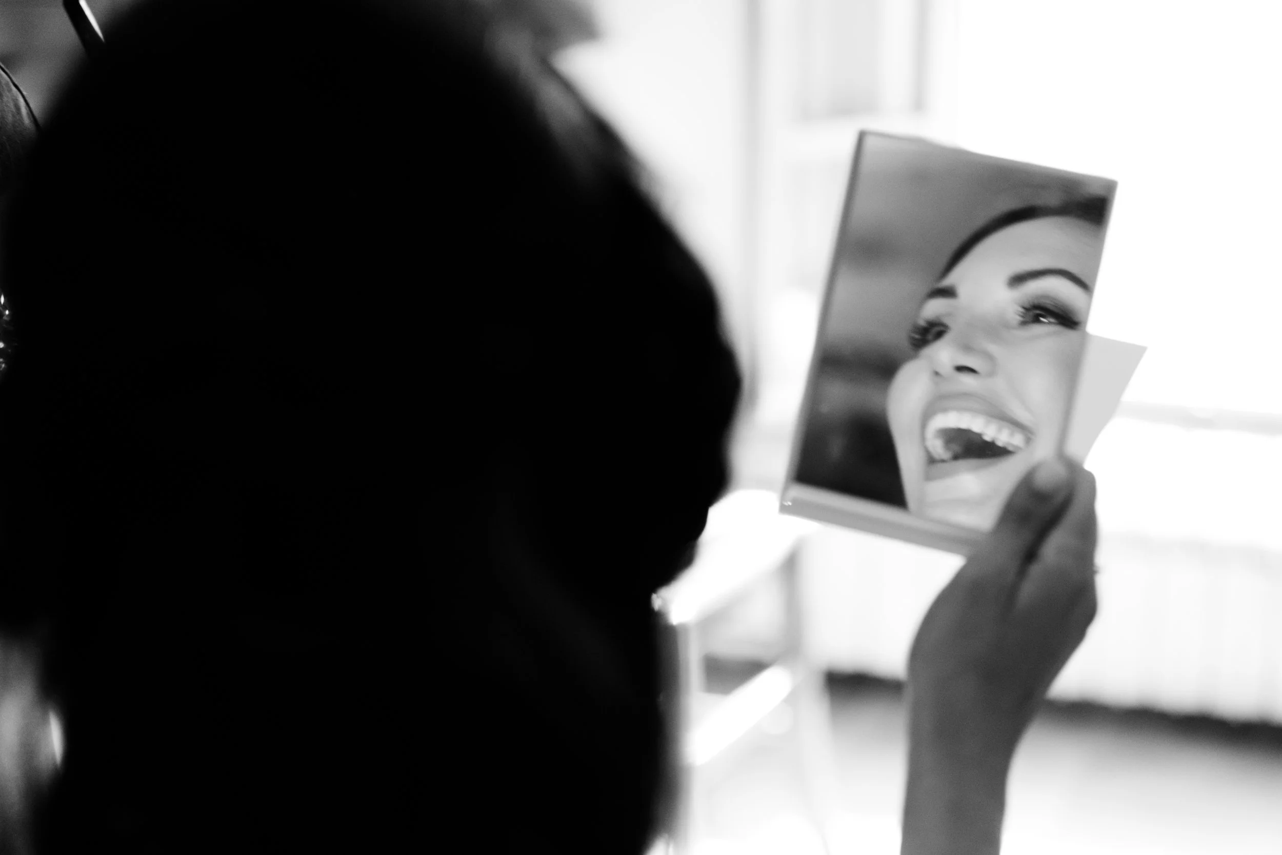 Ragazza che si guarda allo specchio, sorridendo, in una stanza luminosa, in bianco e nero.