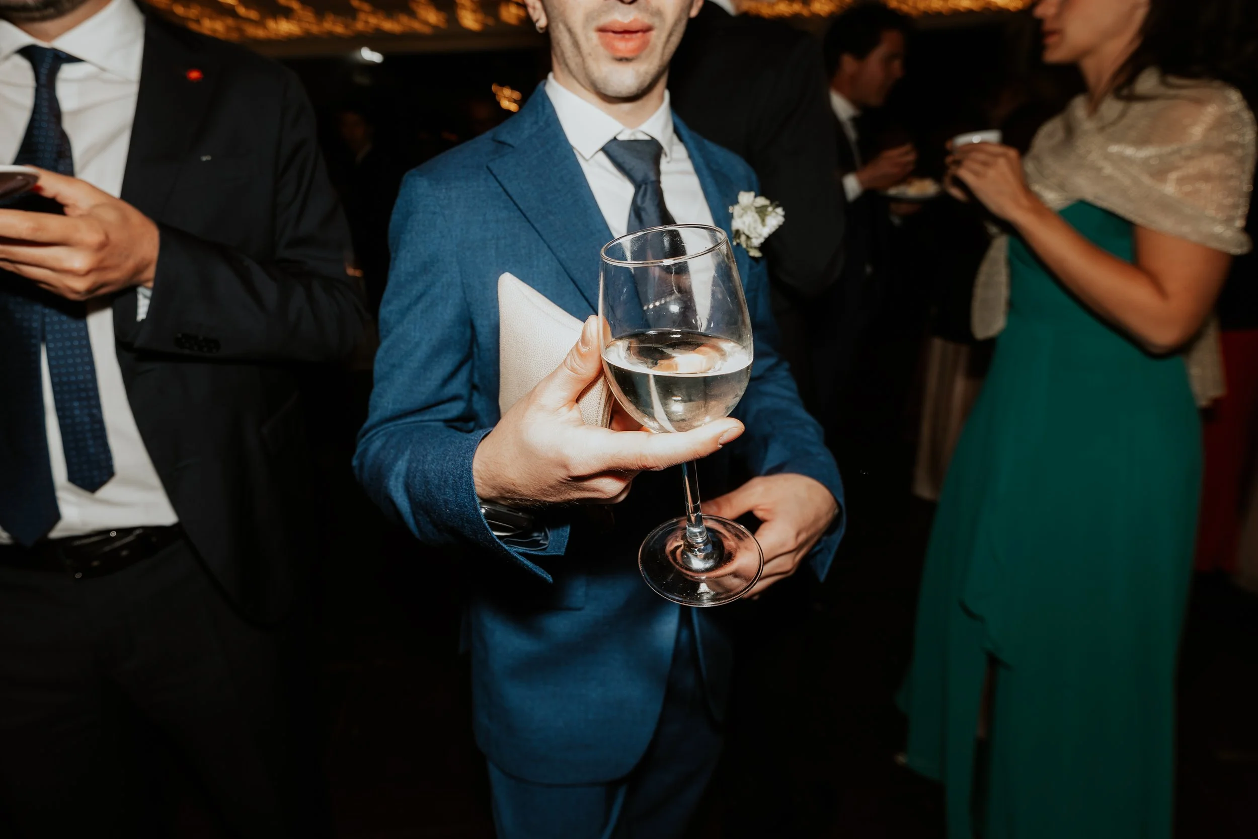 Uomo in abito blu che tiene un calice di vino bianco in un evento sociale