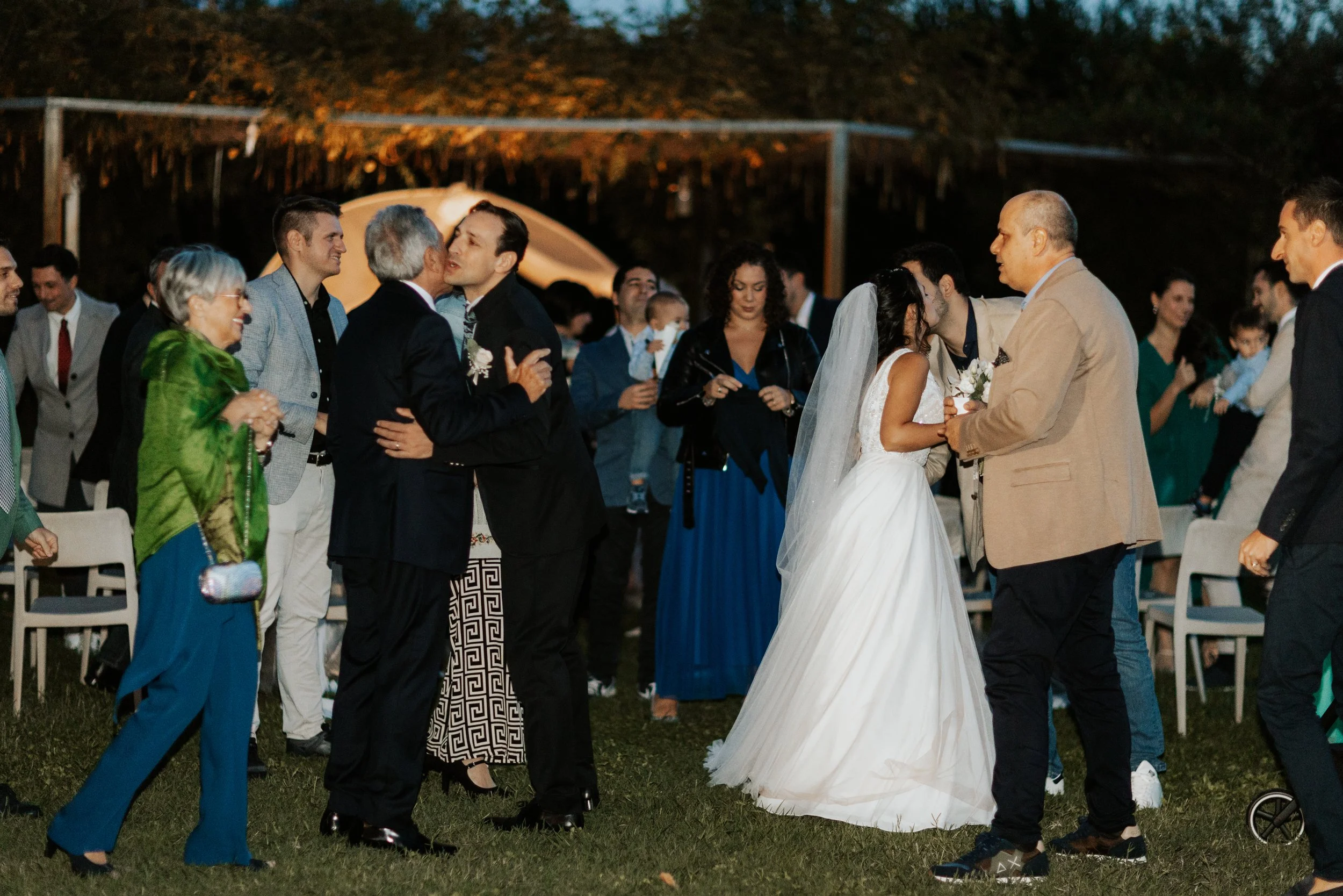 Un matrimonio con gli ospiti che si scambiano baci e abbracci in una cerimonia di nozze all'aperto di sera.