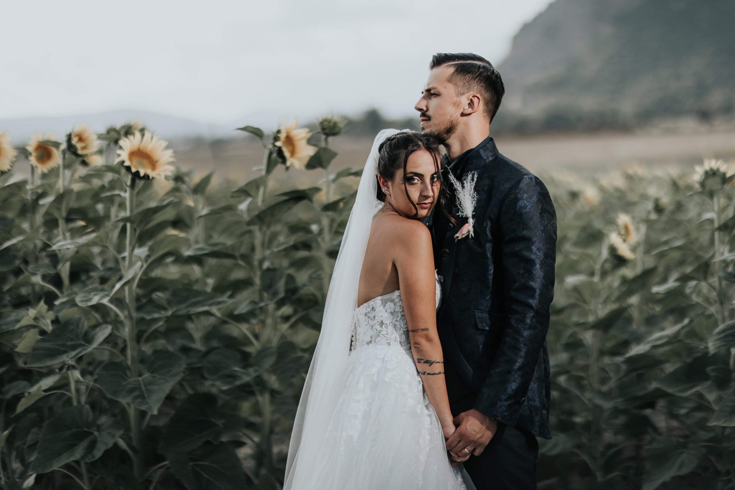 Una coppia di sposi in abiti da matrimonio si abbraccia in un campo di girasoli.
