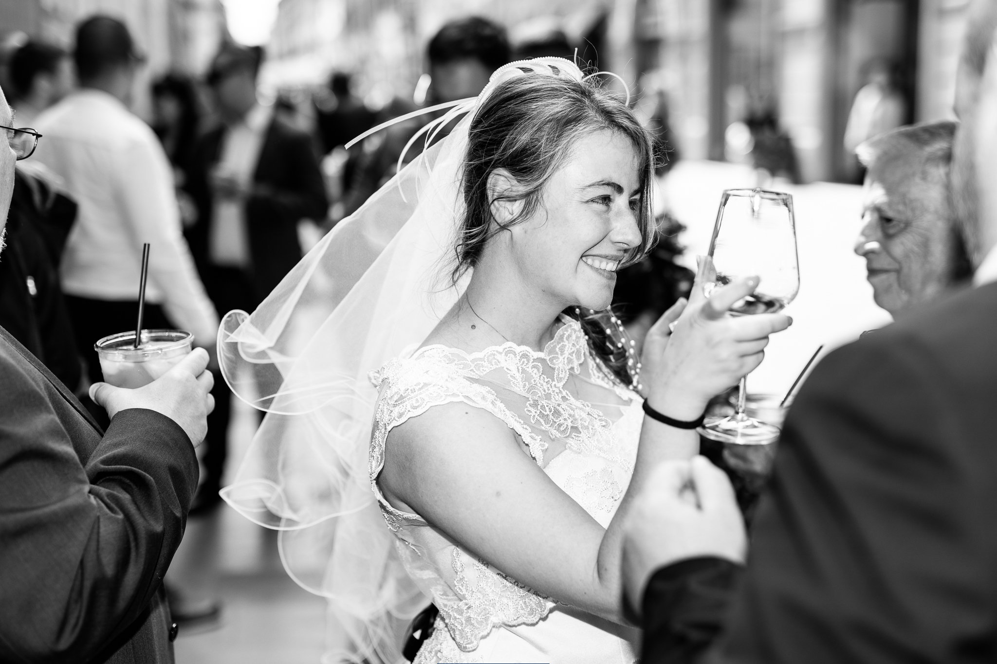 Un ritratto di una sposa sorridente che sorseggia un bicchiere di vino durante un matrimonio, circondata da amici o parenti.