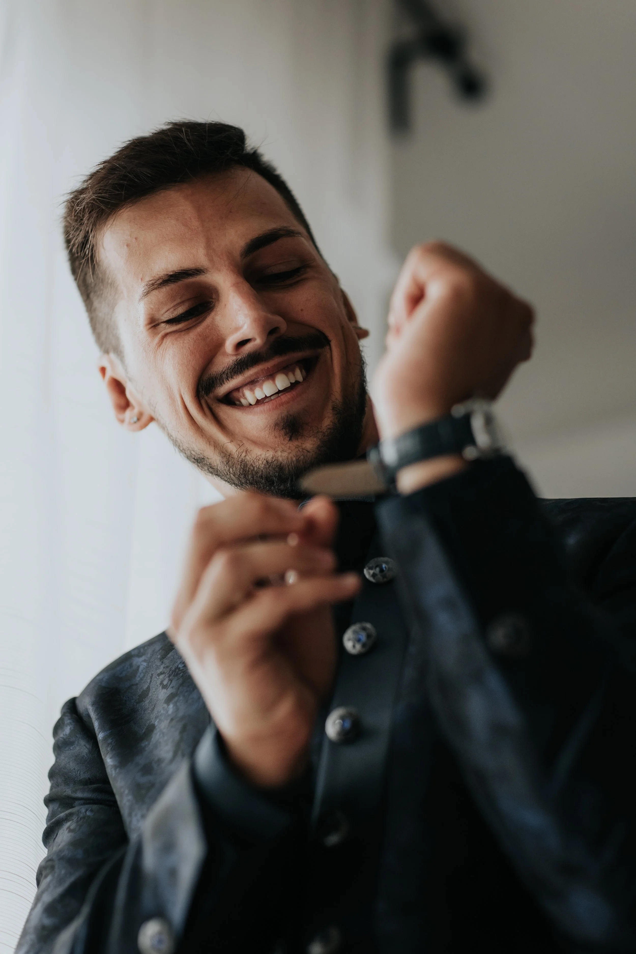 Un uomo sorridente che guarda l'orologio al polso mentre sistema la manica della camicia.
