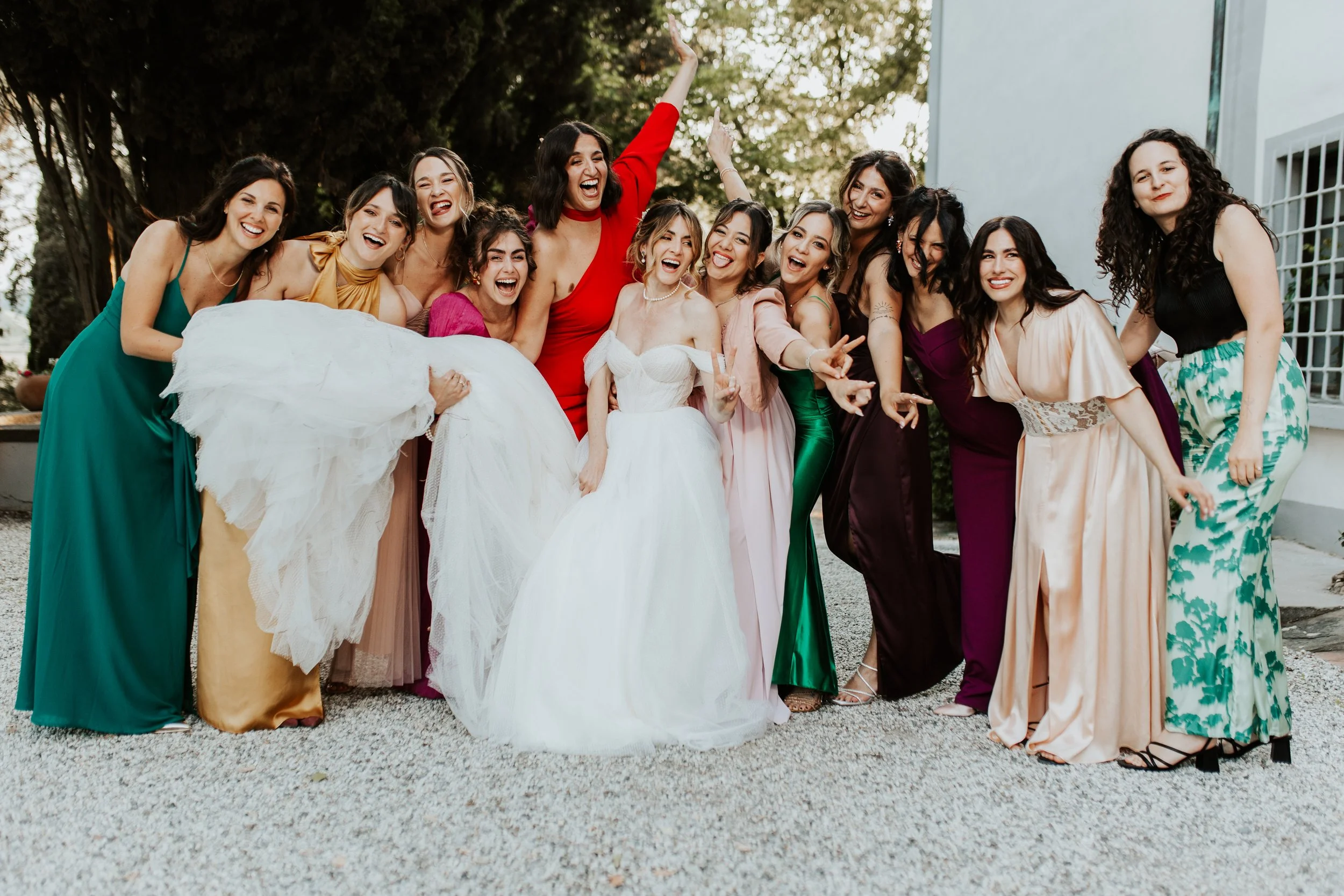 Gruppo di donne sorridenti, alcune in abiti da sera colorati, che ridono e fanno festa all'aperto.