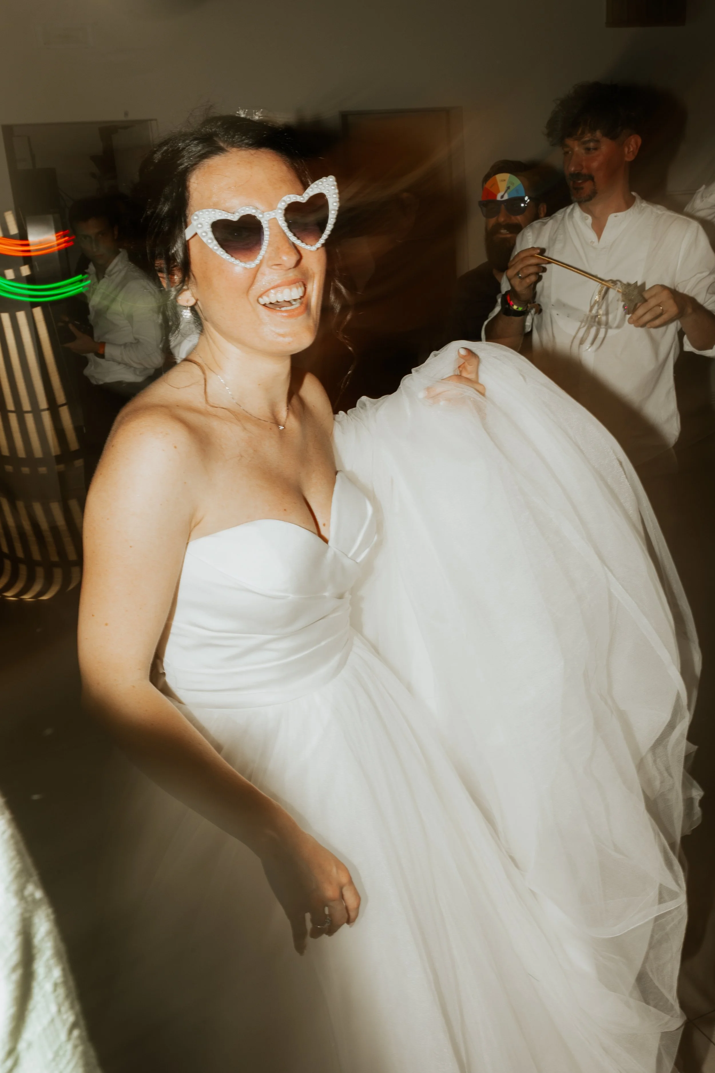 Sposa con occhiali a cuore in festa e amici sullo sfondo