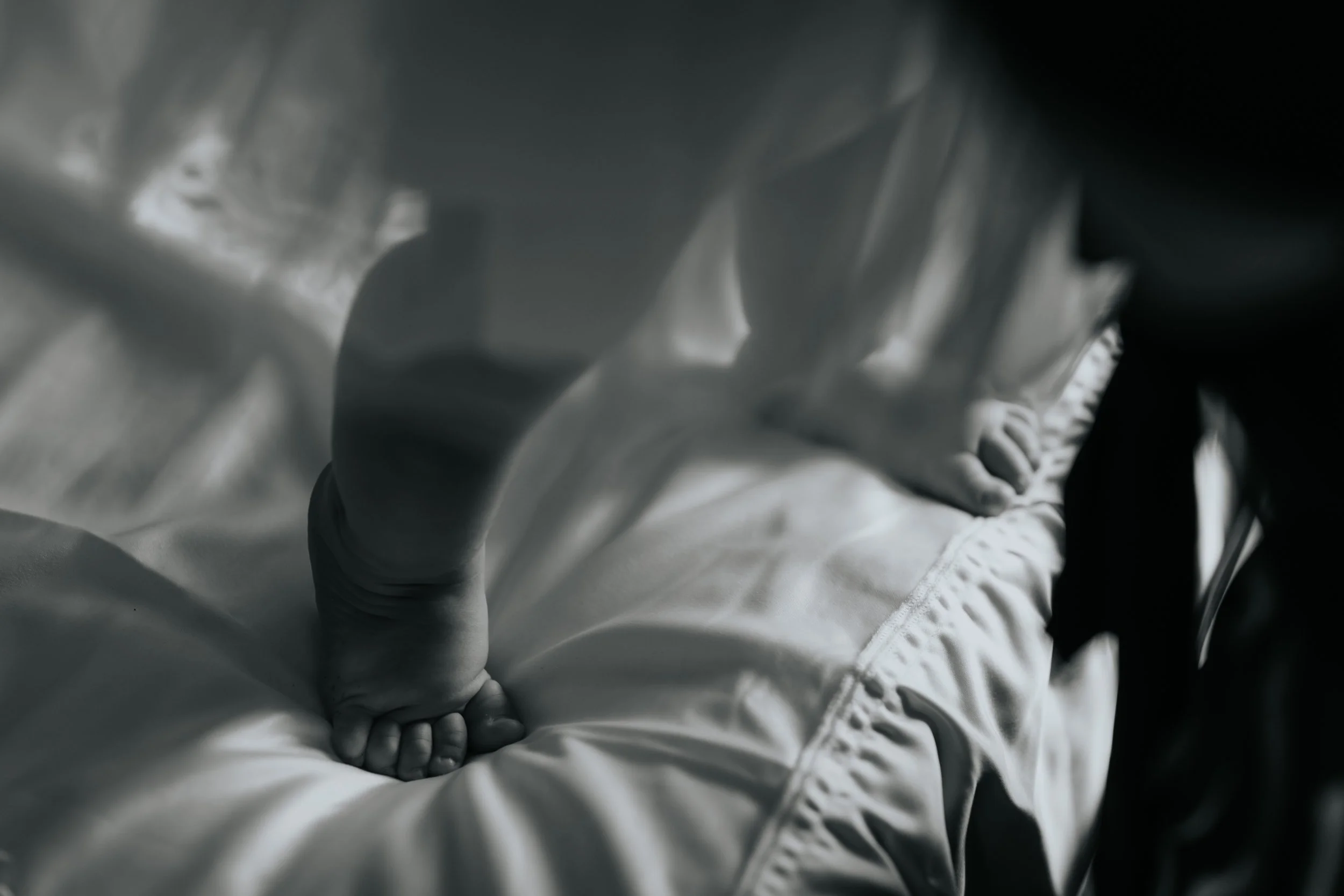 Mano di un bambino che si aggrappa a un lenzuolo su un letto.