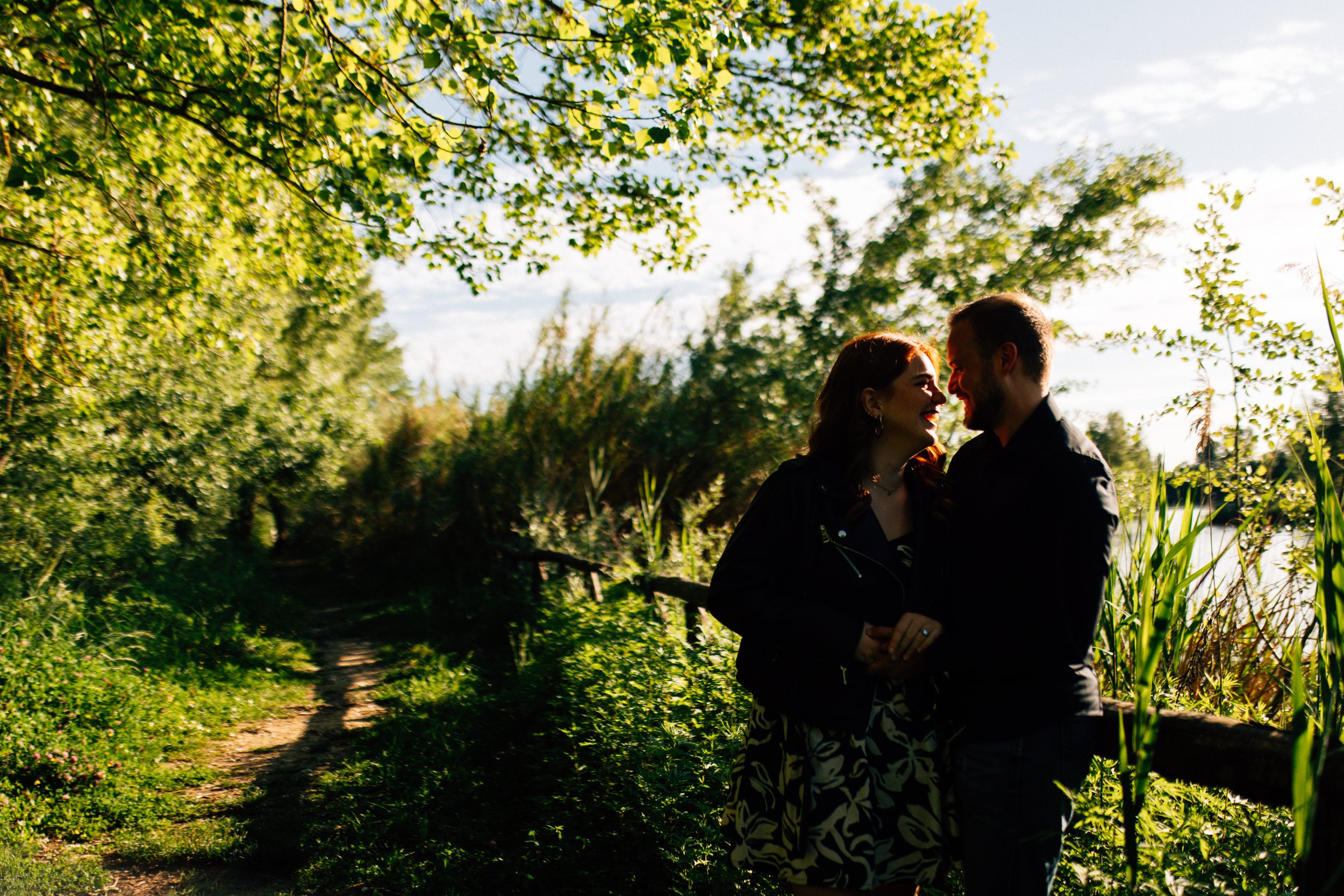 Una coppia felice si abbraccia e sorride in un bosco verde, con il sole che splende attraverso gli alberi.