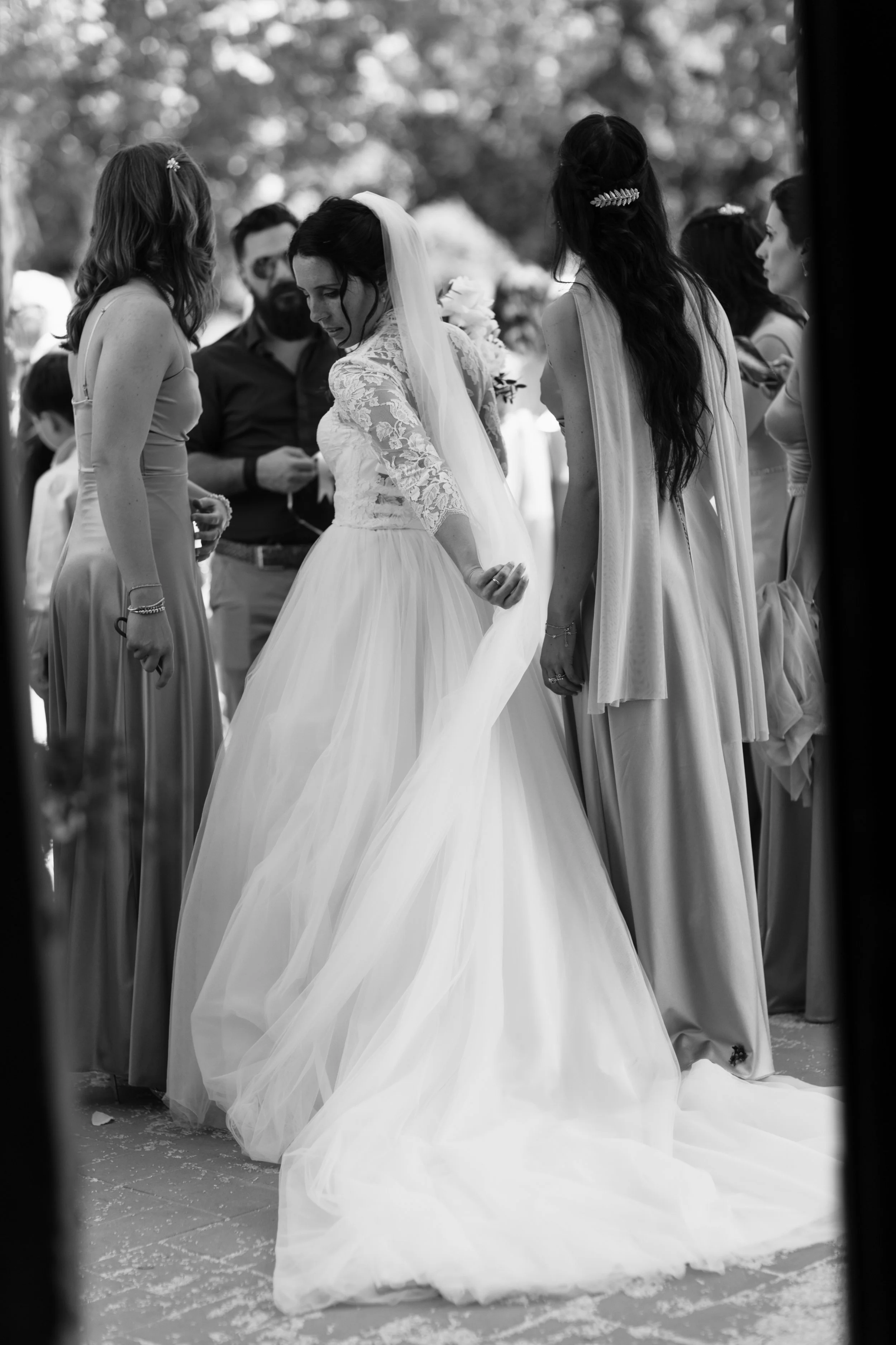 Una sposa in abito da matrimonio circondata da amiche durante il matrimonio. In bianco e nero.