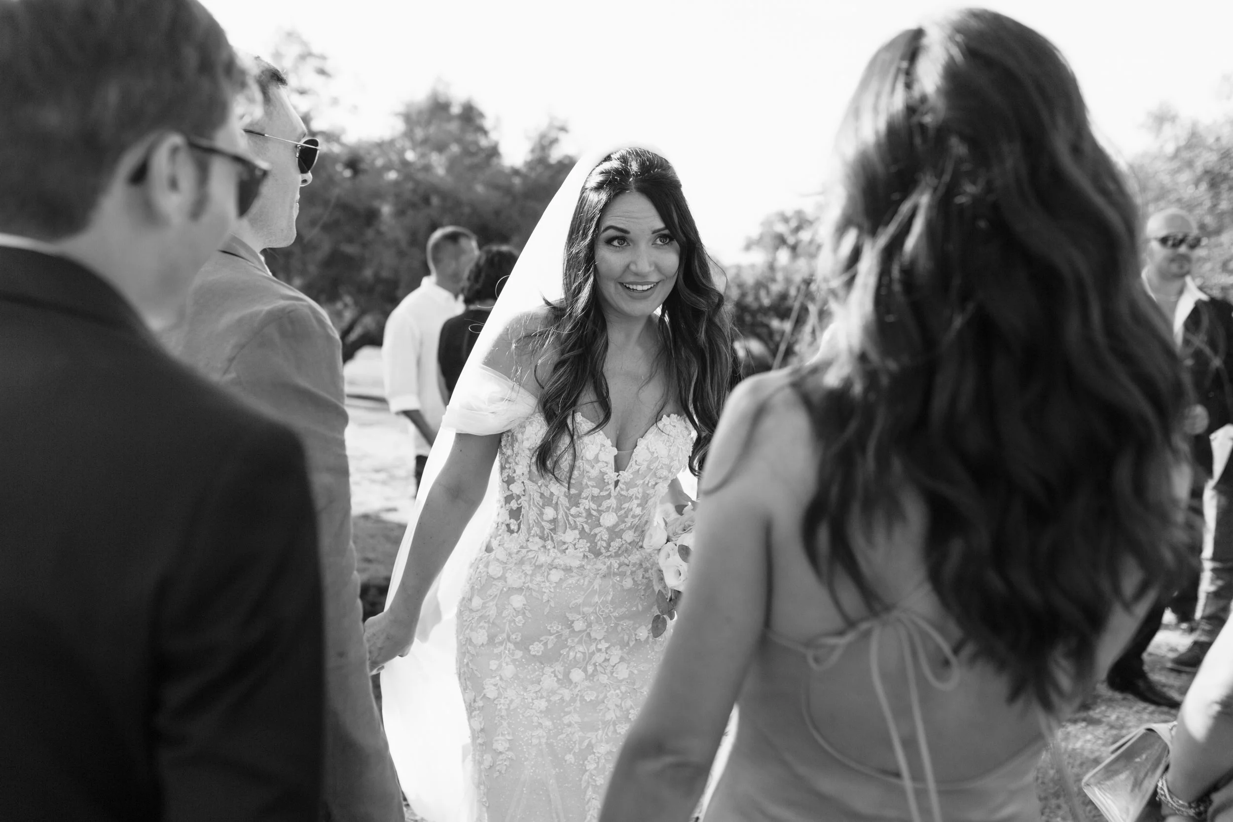Una sposa sorridente in abito da matrimonio si trova circondata da amici in un matrimonio all'aperto.