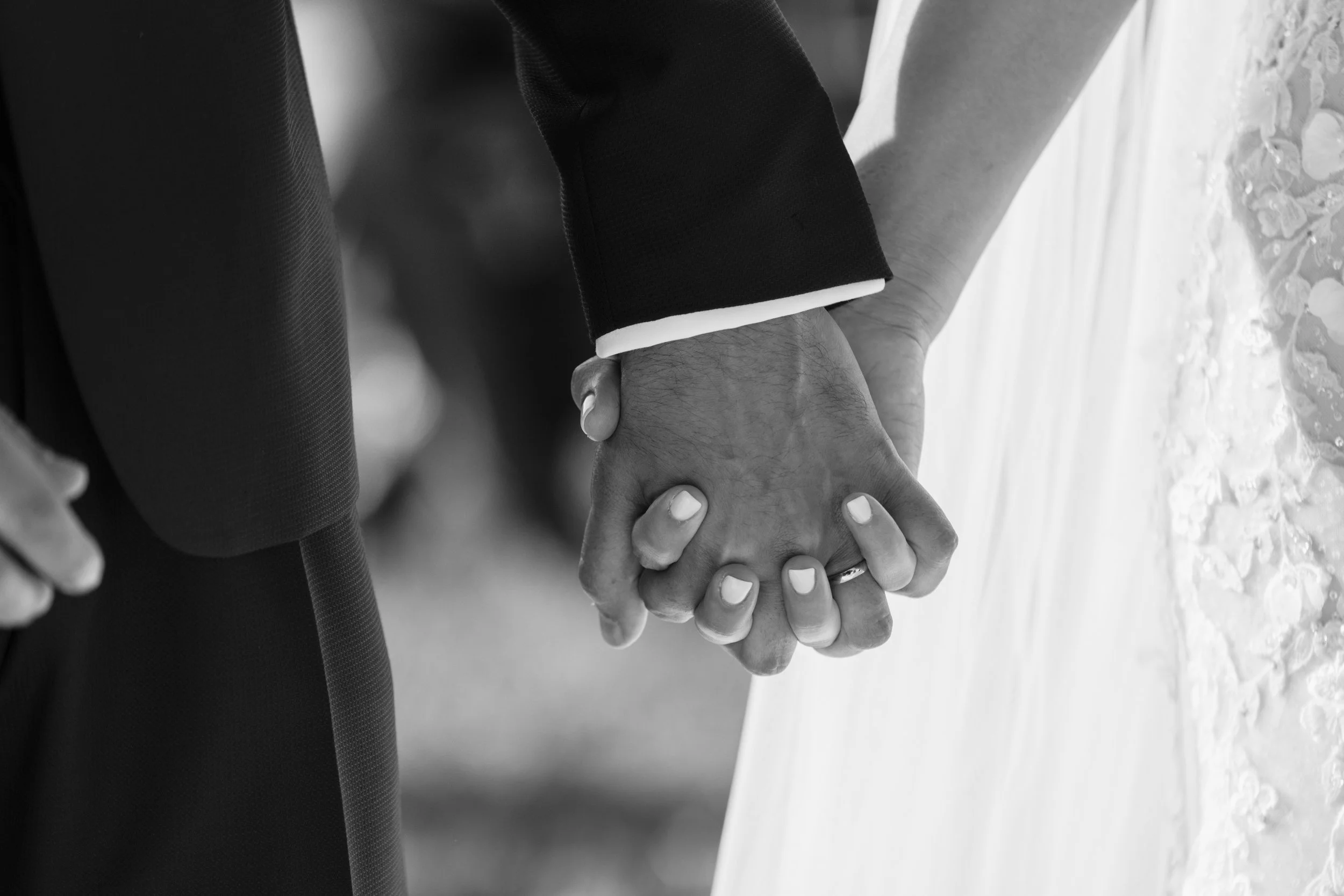 Due persone che tengono le mani intrecciate, probabilmente durante un matrimonio, con abiti eleganti e abito da sposa.