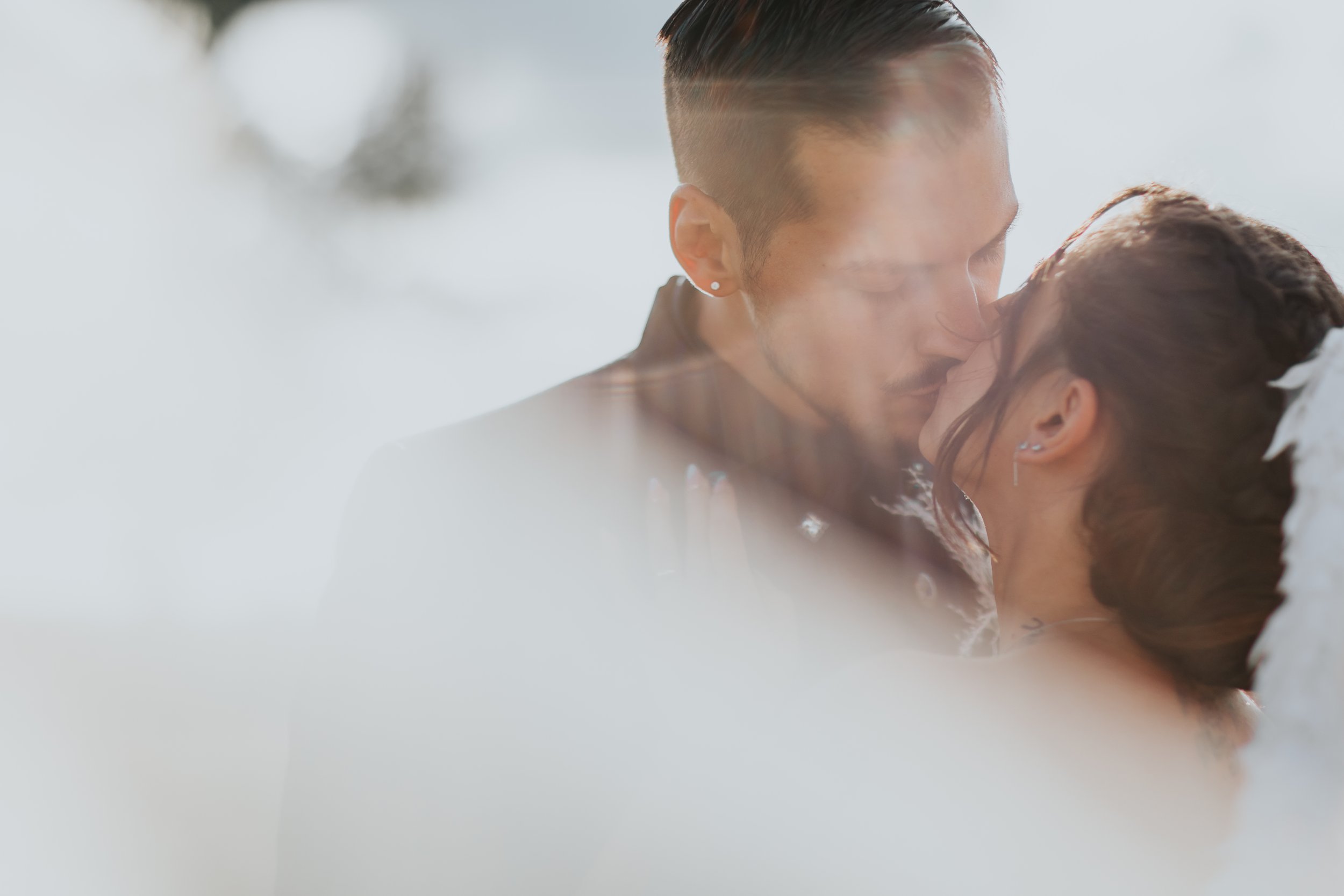 Due persone si baciano intimamente, sfiorandosi il volto, con un'illuminazione naturale e uno sfondo sfocato.