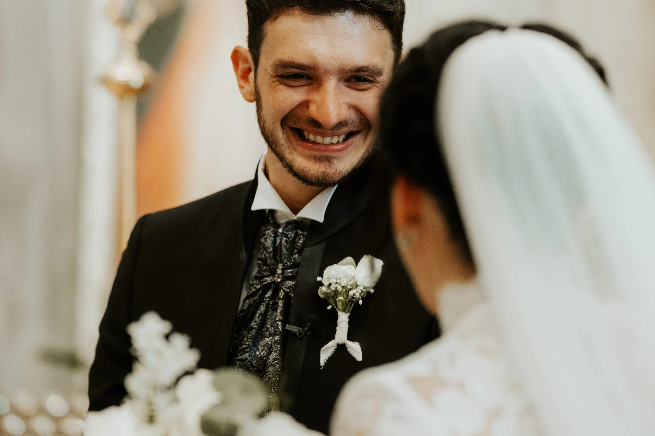 Sposo sorridente che guarda la sposa durante il matrimonio, entrambi vestiti elegantemente.