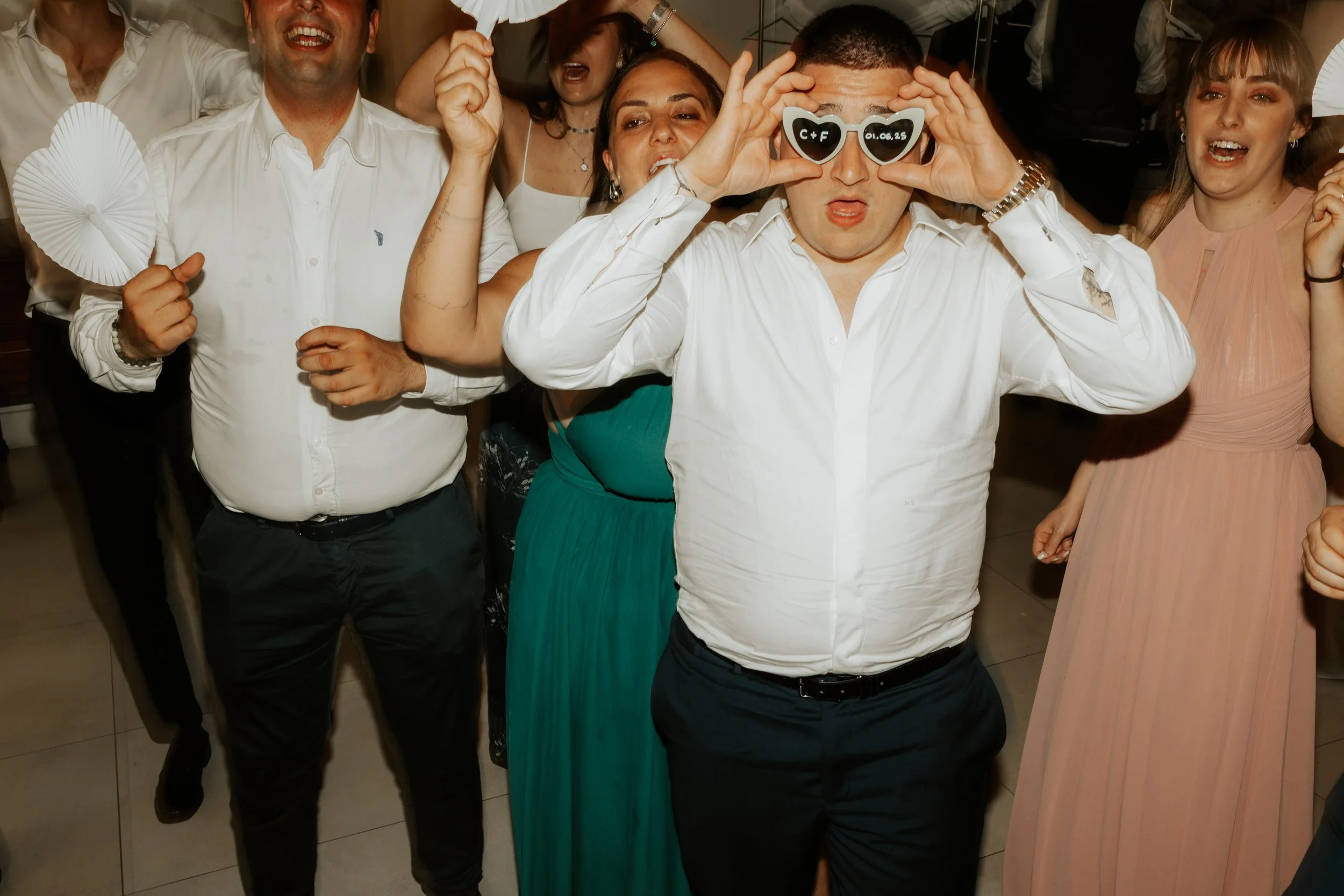 Gruppo di persone che si divertono alla festa, alcune indossano occhiali divertenti e fanno gesti scherzosi.