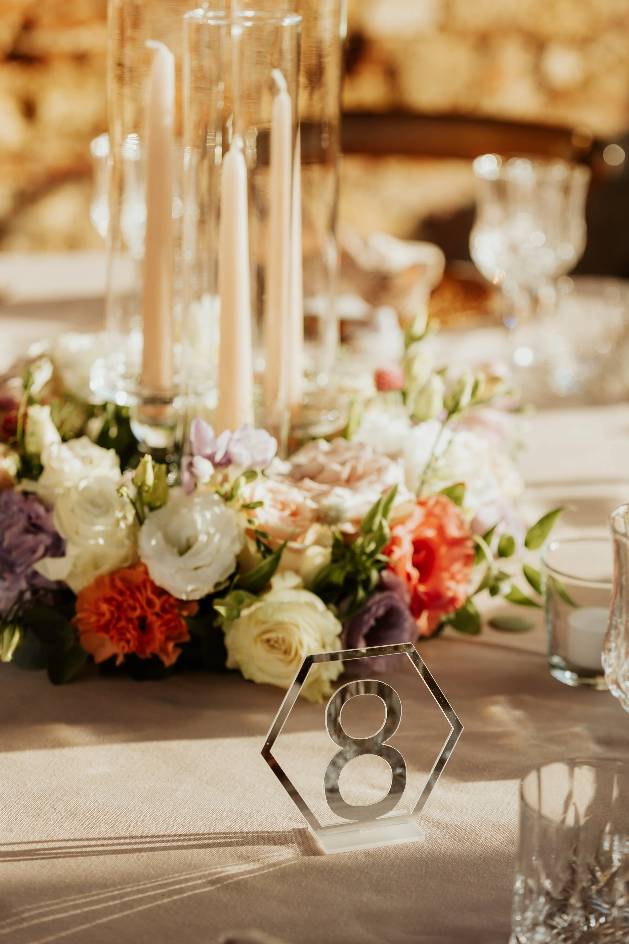 Tavola decorata con fiori e candele, numero di tavolo 8 in vetro trasparente.