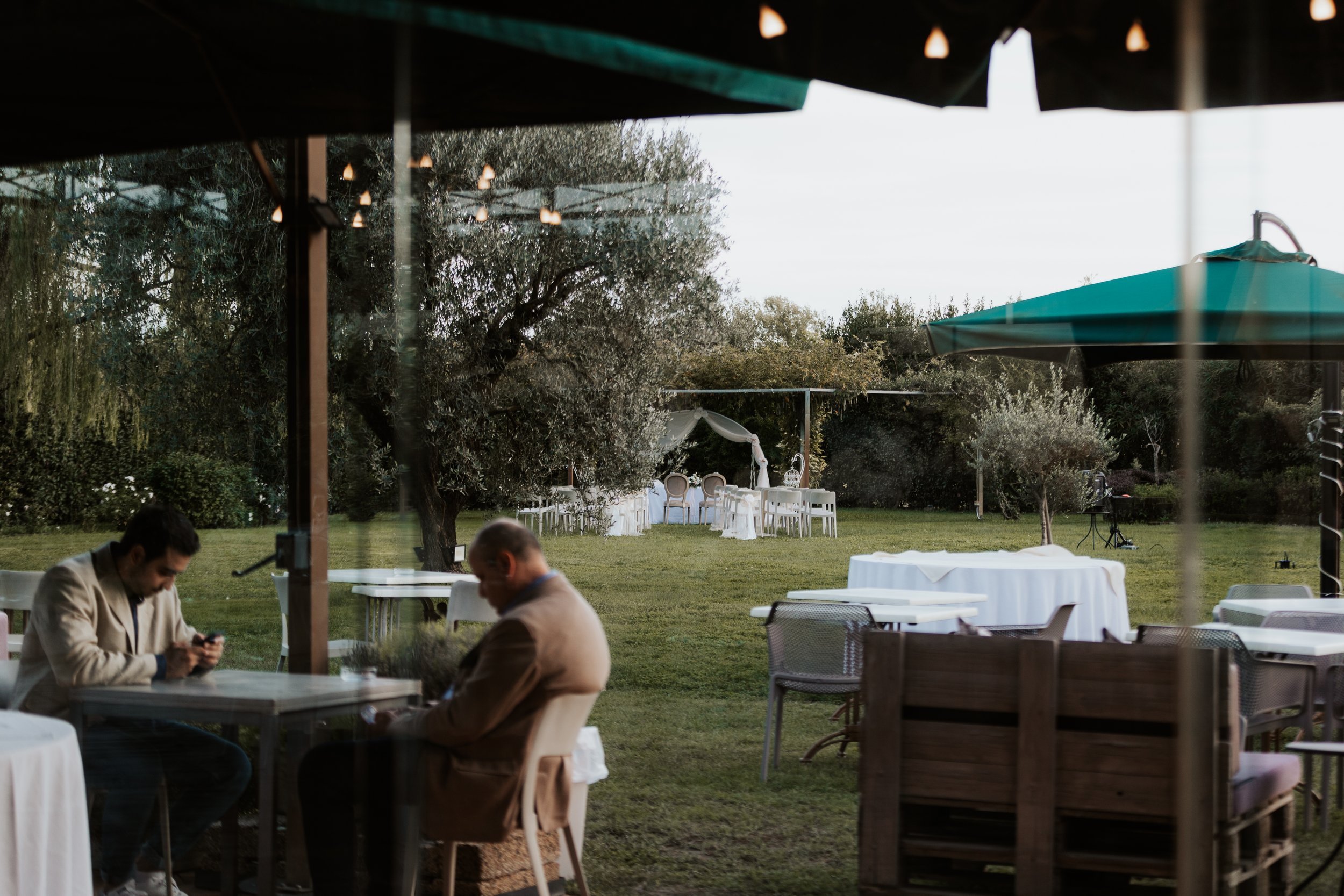 Spazi esterni di un luogo di eventi con tavoli e sedie, alberi e ombrelloni, in attesa di un ricevimento o festa.