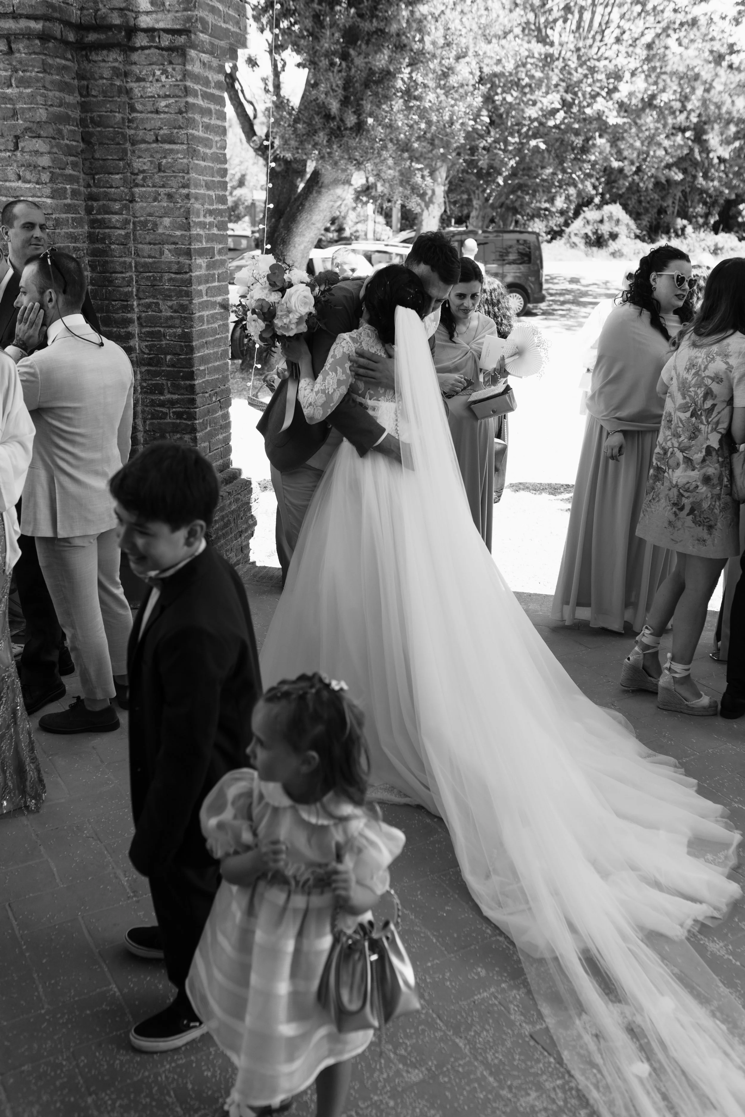 Una coppia di sposi si abbraccia davanti a una chiesa, circondata da amici e parenti, durante il matrimonio.